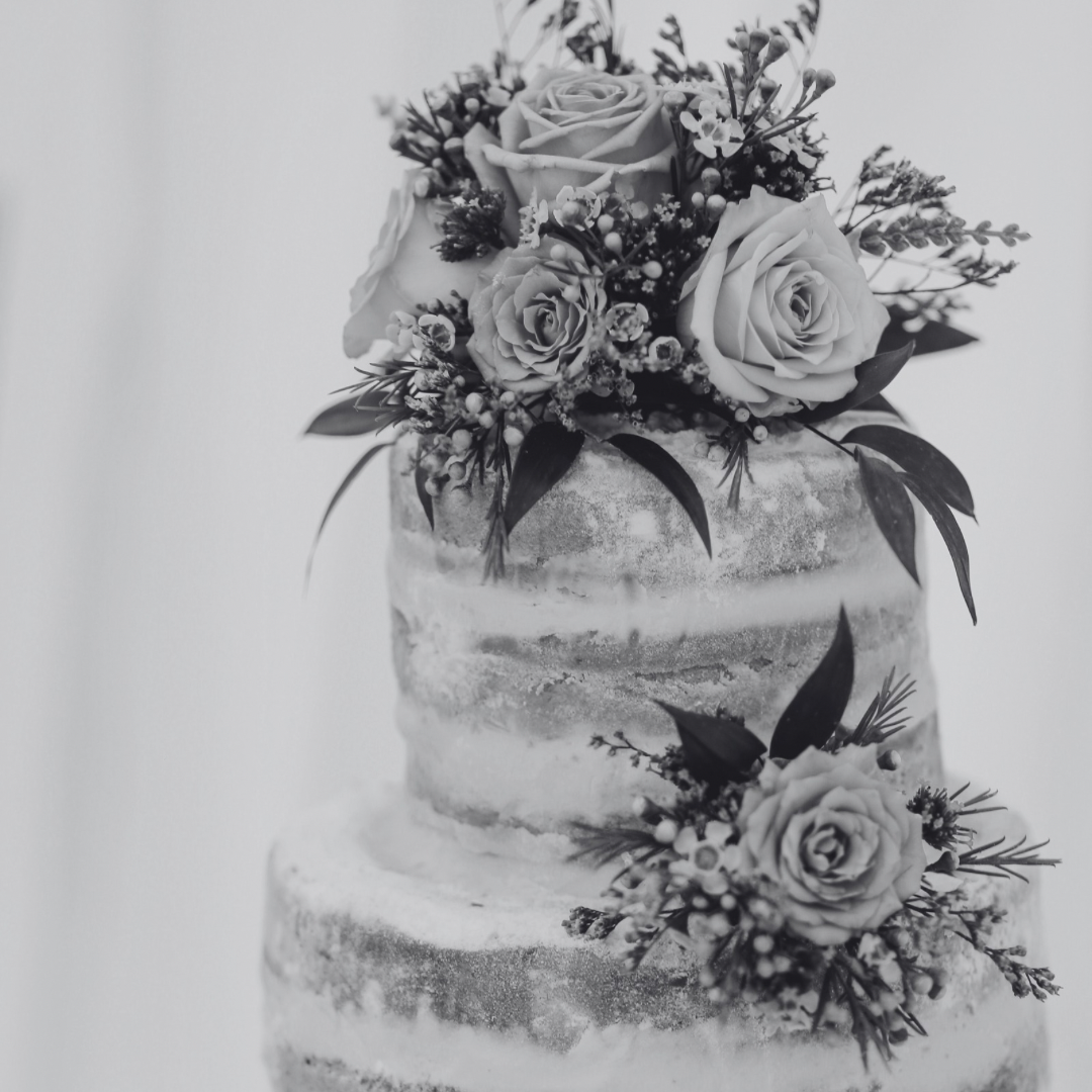 A black and white photo of a three-tiered cake decorated with fresh roses and greenery.