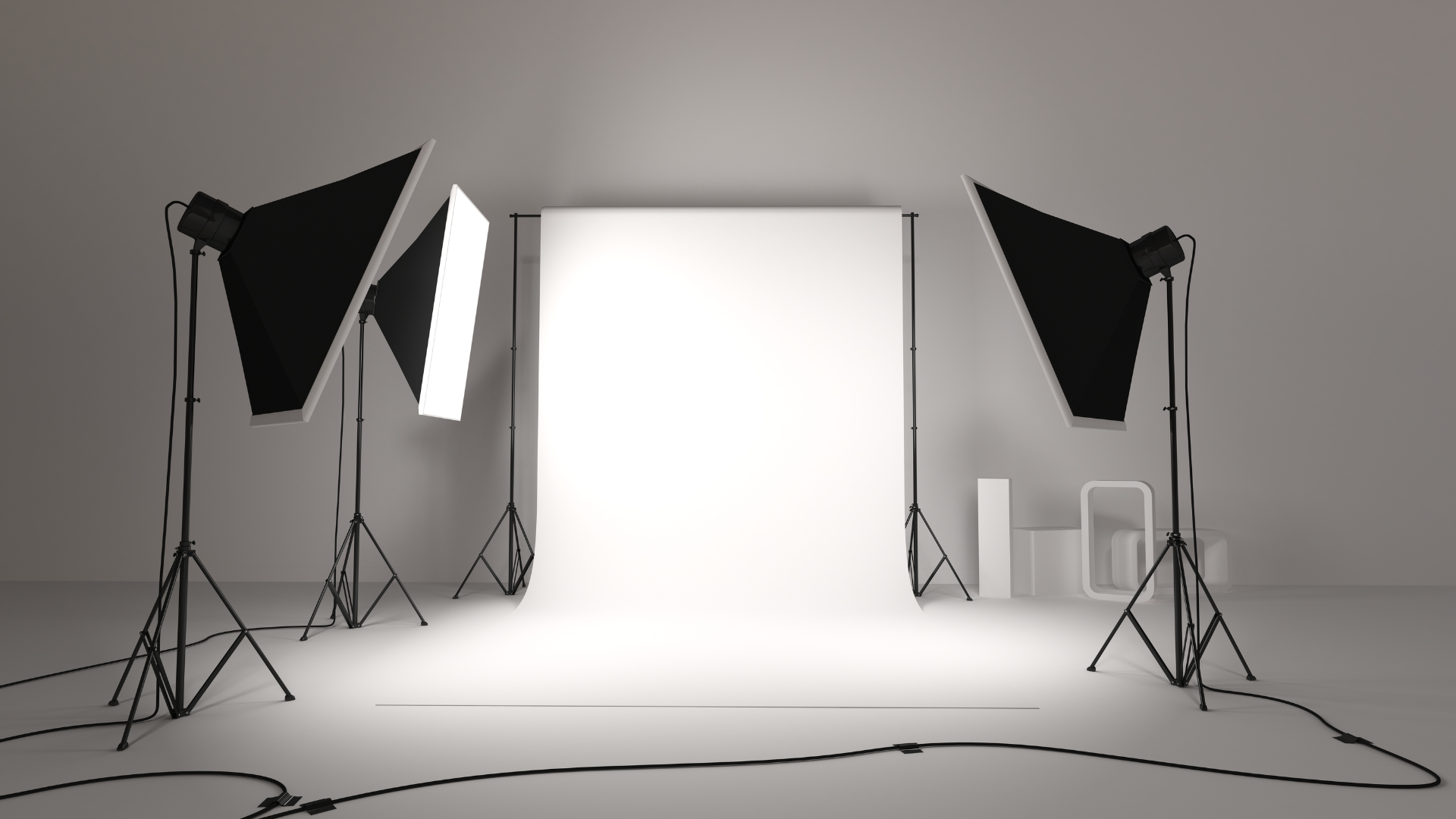 Photo of a professional studio with 3 large softbox lights, a white backdrop, and studio equipment against a gray wall.