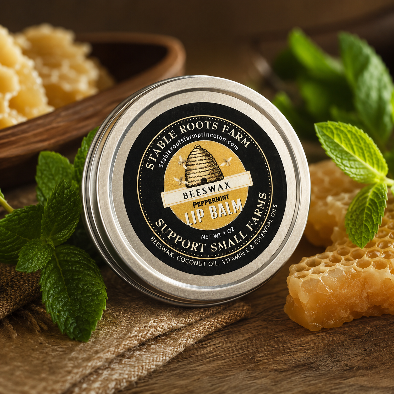 A tin of Stabile Roots Farm peppermint beeswax lip balm surrounded by fresh mint leaves, honeycomb, and a wooden bowl of honey on a rustic wooden surface.