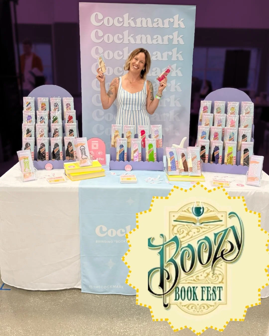 A woman standing behind a table displaying various colorful books at a book festival, with a large sign that says "Book Fest."