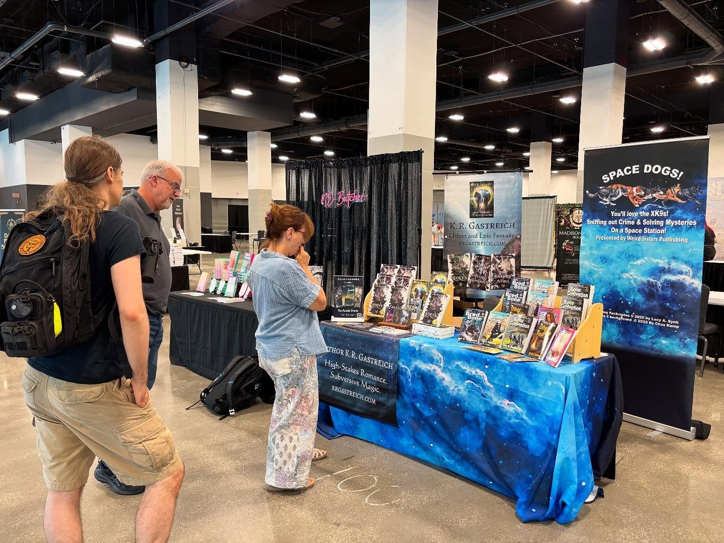 People browsing at a book signing booth for author K.R. Gastreich, showcasing books and a space-themed banner titled 'Space Dogs!'