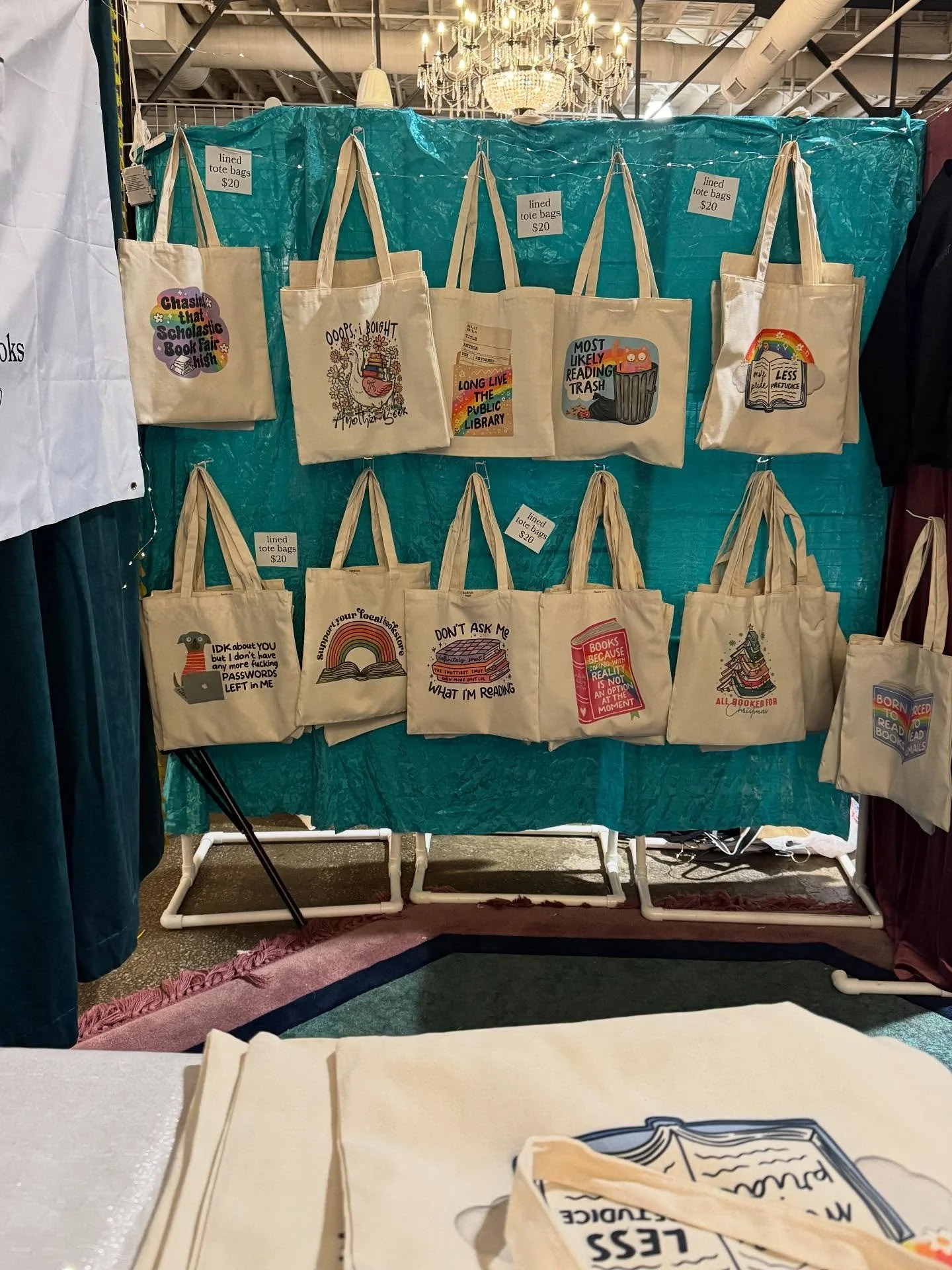 Display of tote bags with humorous book-related prints hanging on a blue background in a store or market setting.