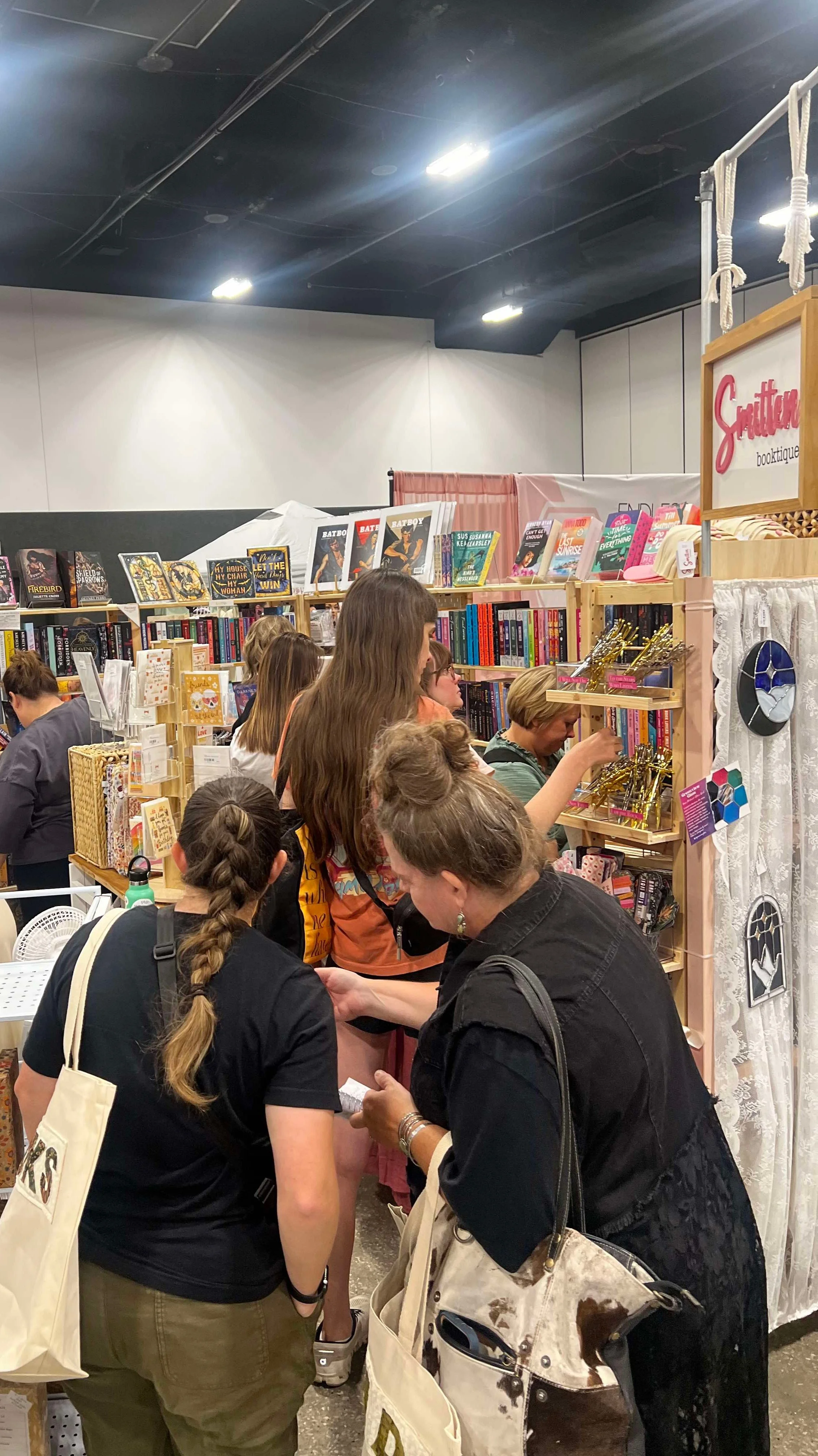 People shopping at a crowded bookstore booth with shelves of books and decorative items.