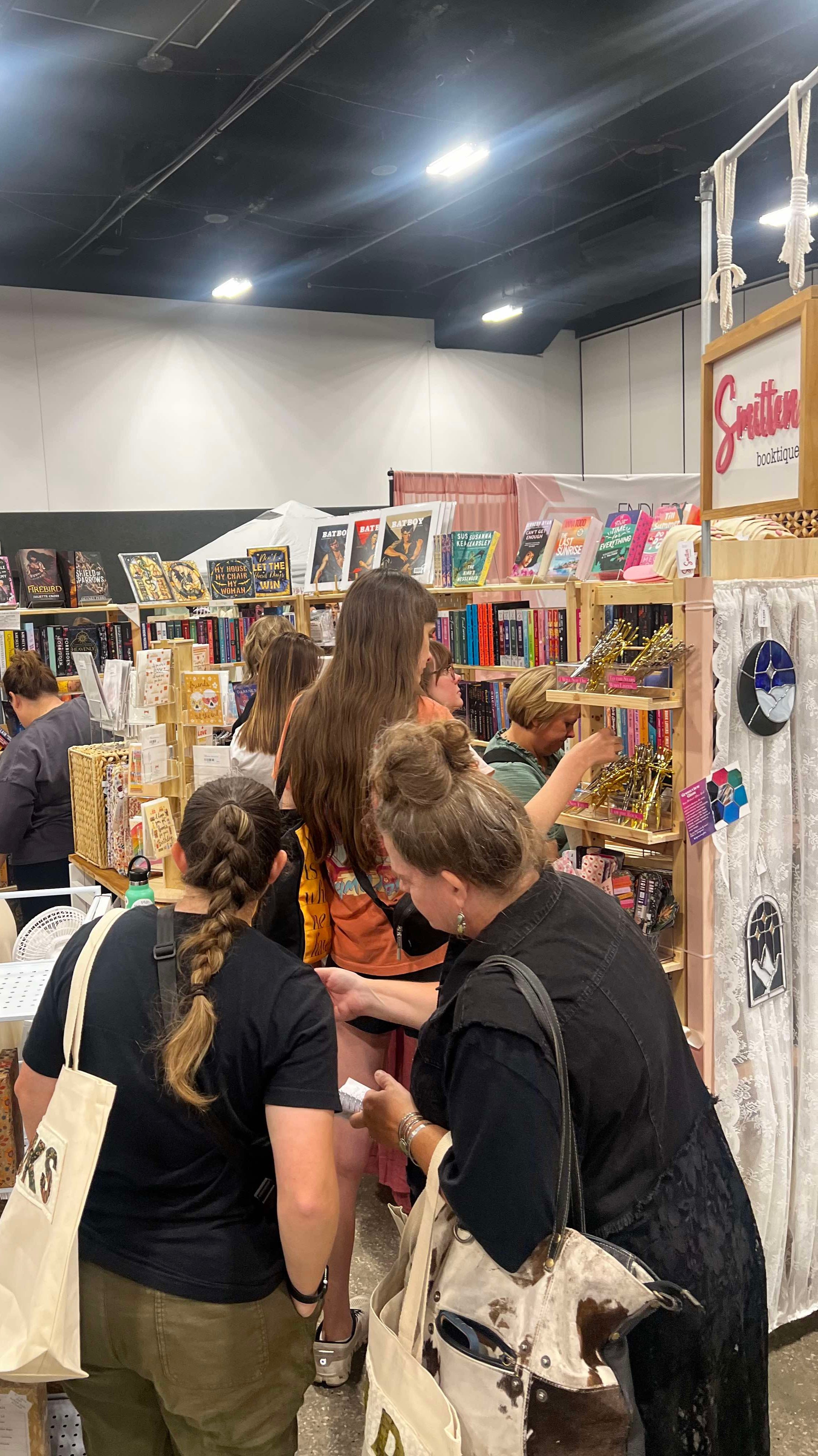 Crowded bookstore booth with women browsing and shopping, bookshelves filled with books, and a sign that reads 'Gritfond'.