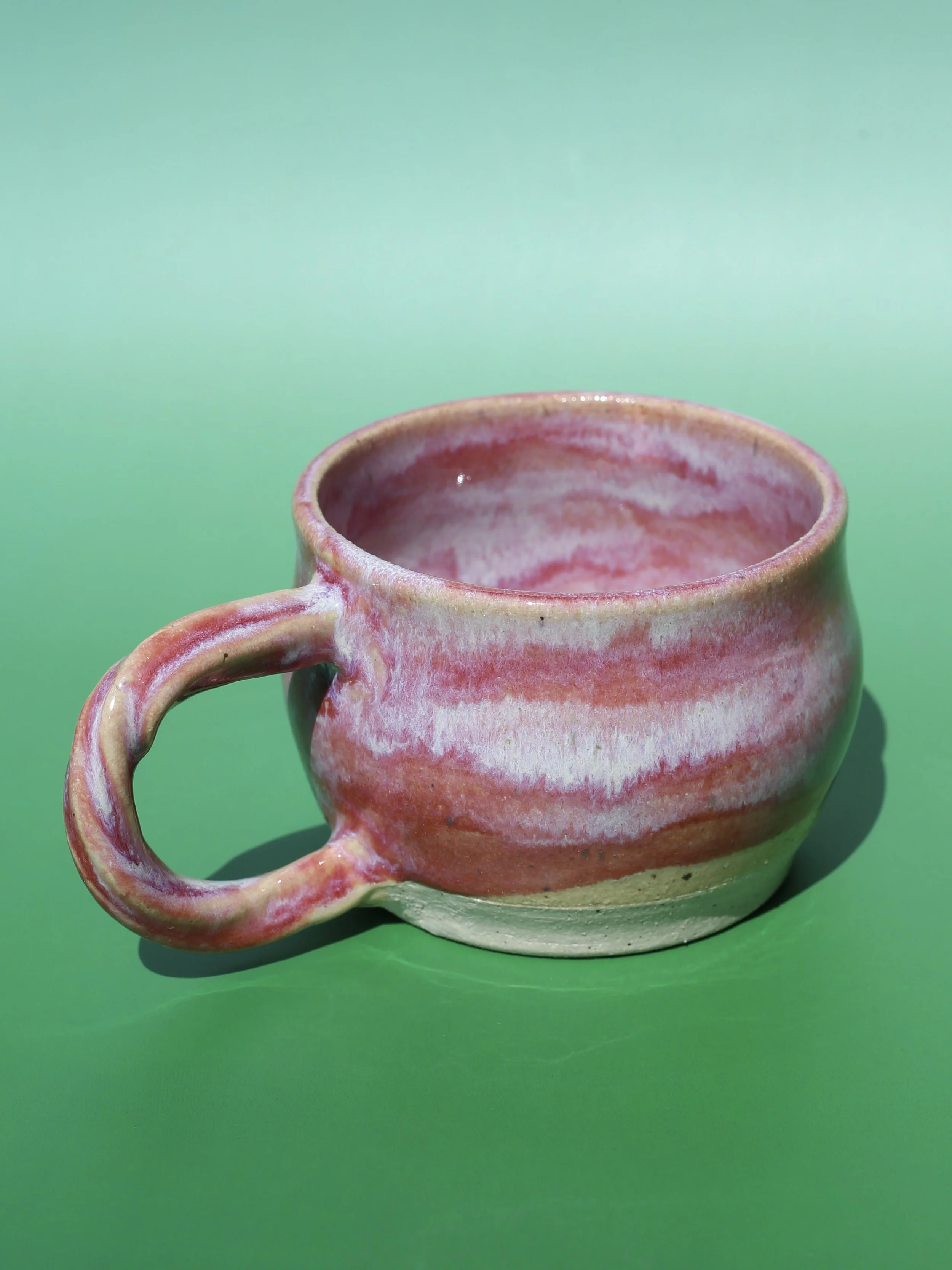 A handmade vibrant ceramic mug with a marbled pink and white finish resting on a green surface.