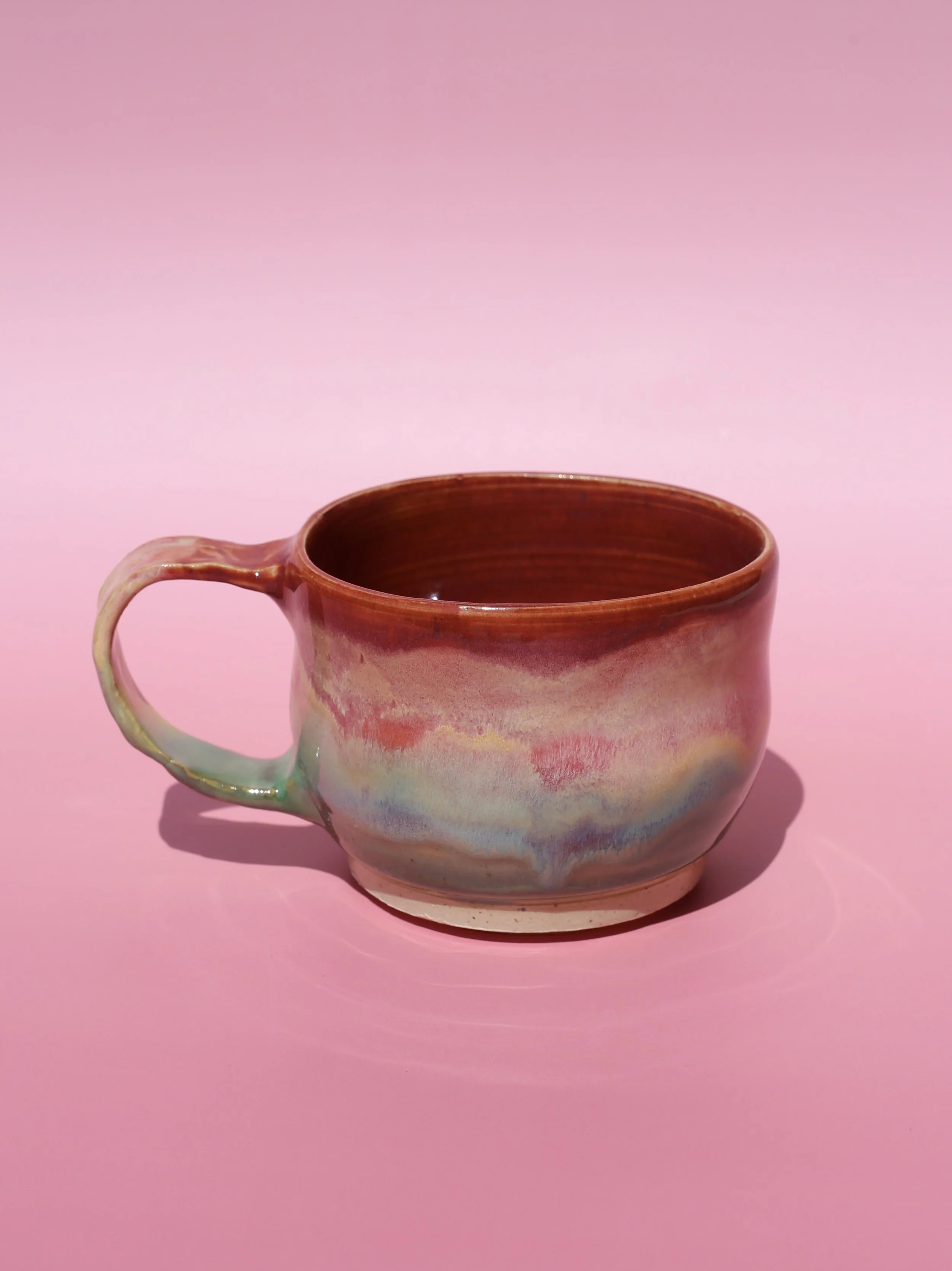 A ceramic mug with swirling pastel colors on a pink background.