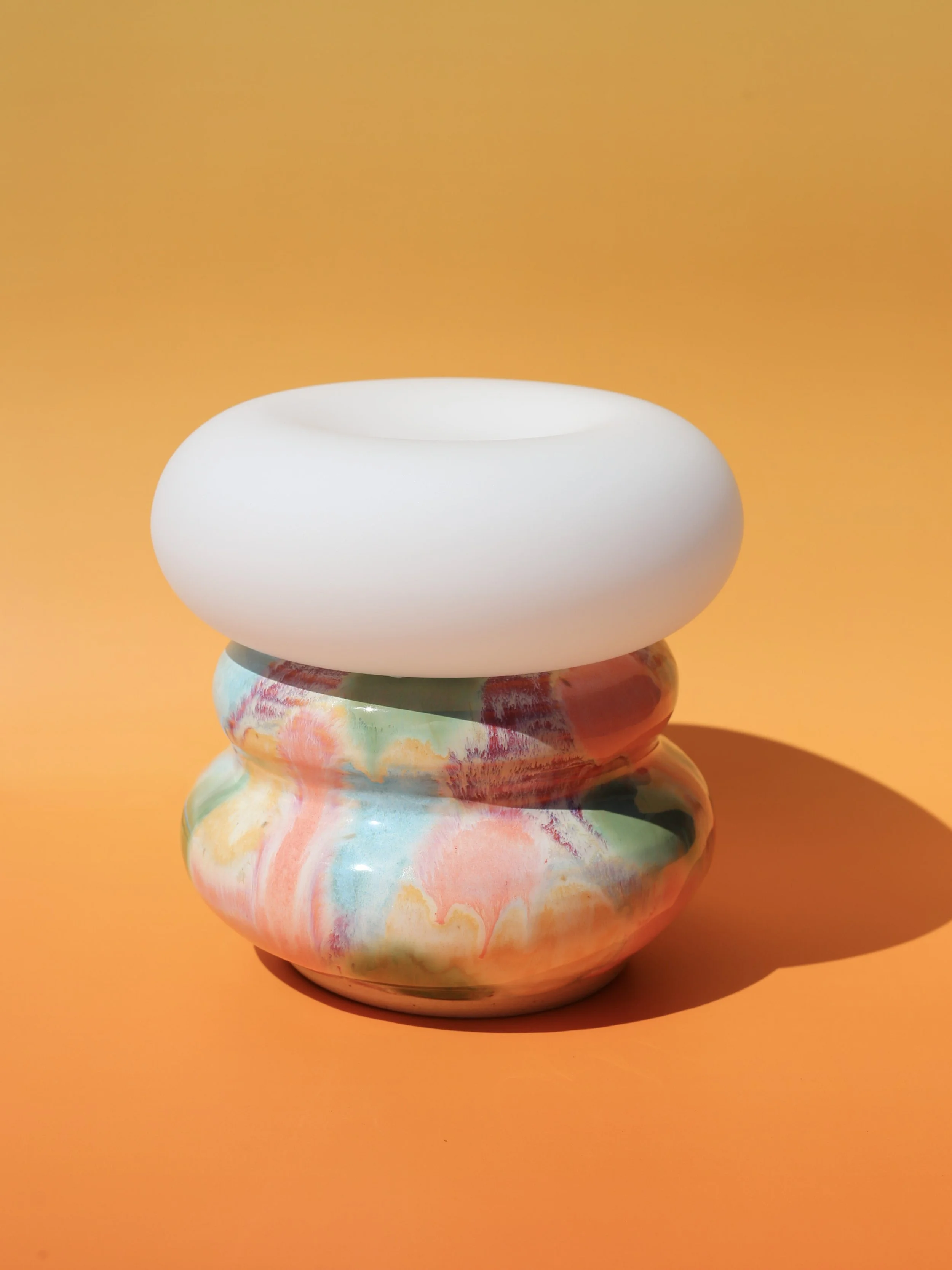 Handmade ceramic lamp with a marbled lamp base and donut lightbulb with pastel colors against an orange background.