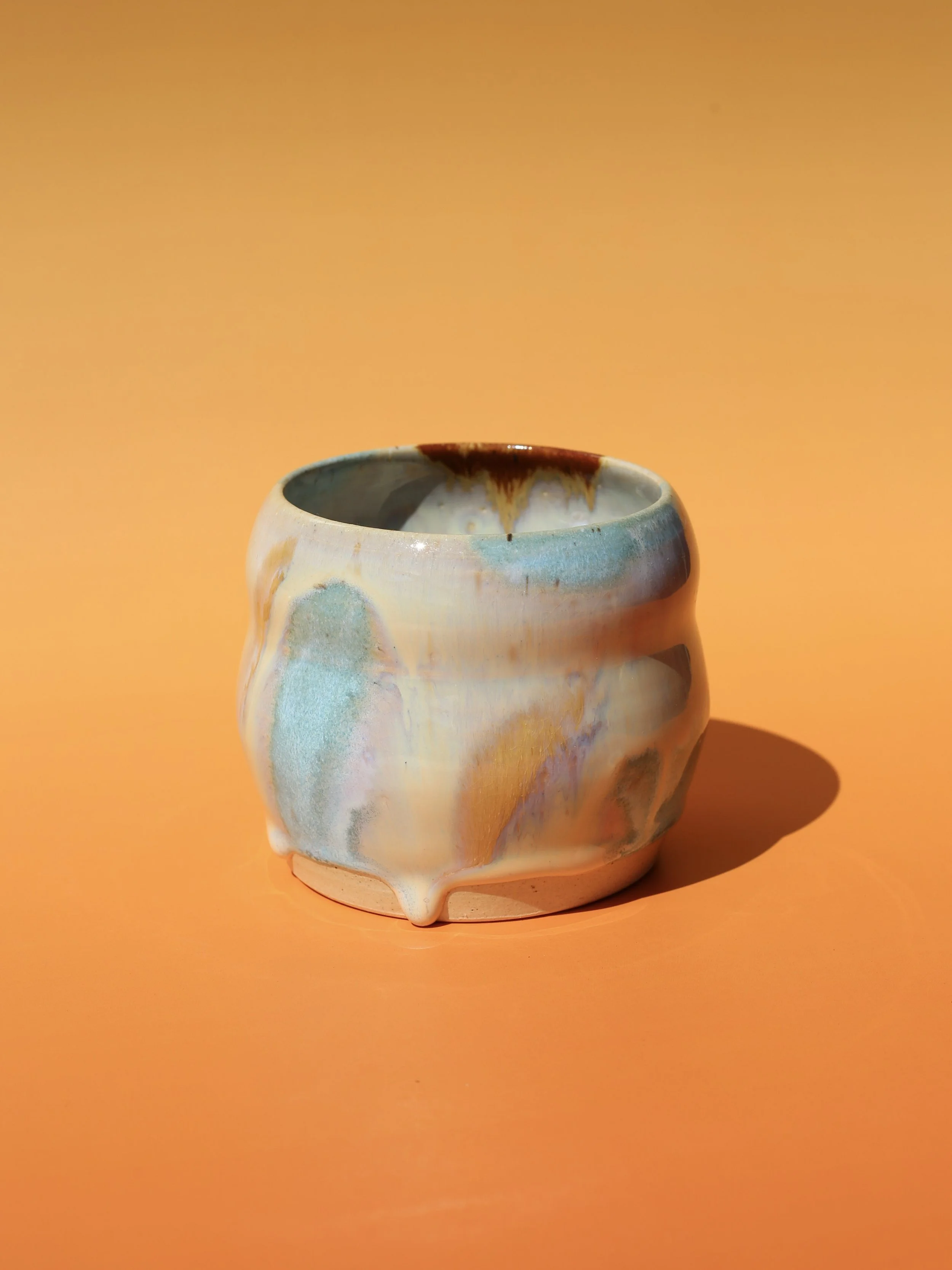 A small ceramic vase with pastel colors and a drip glaze design, set against an orange background.