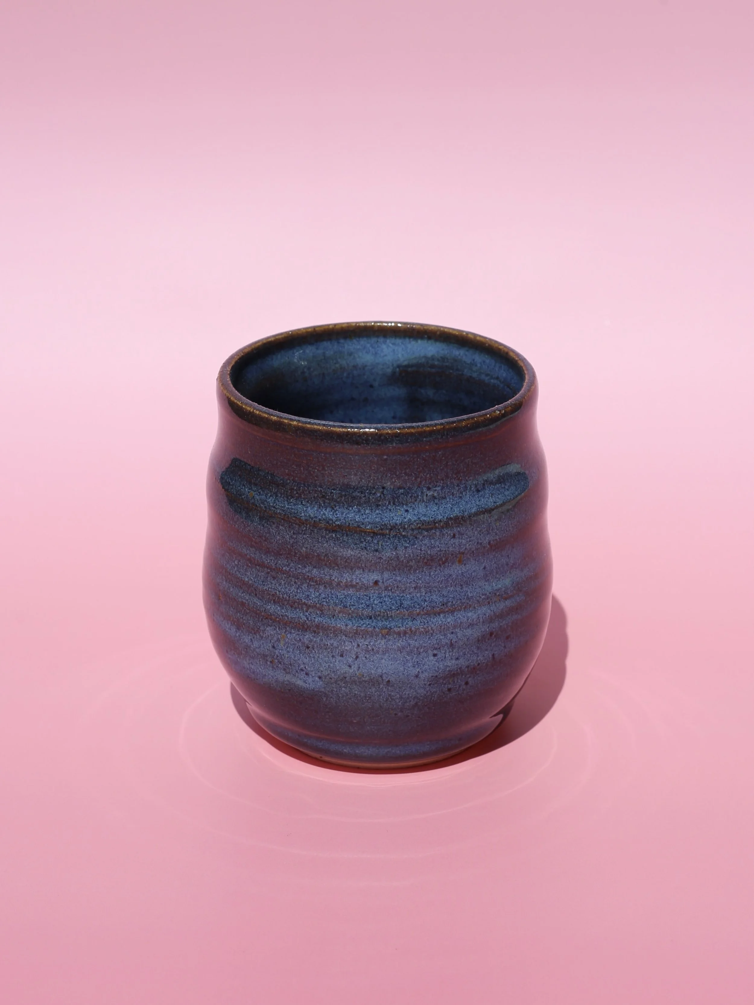 A ceramic vase with horizontal blue and dark brown stripes on a pink background.