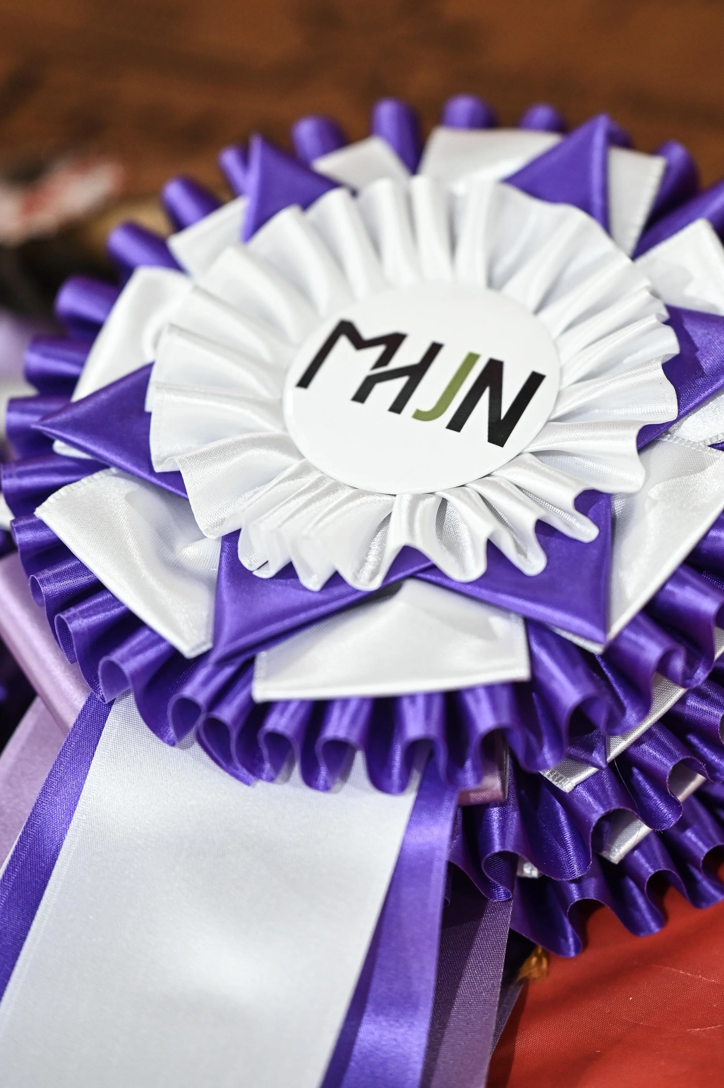 Close-up of a purple, white, and black rosette ribbon with the initials 'MHJN' in the center.