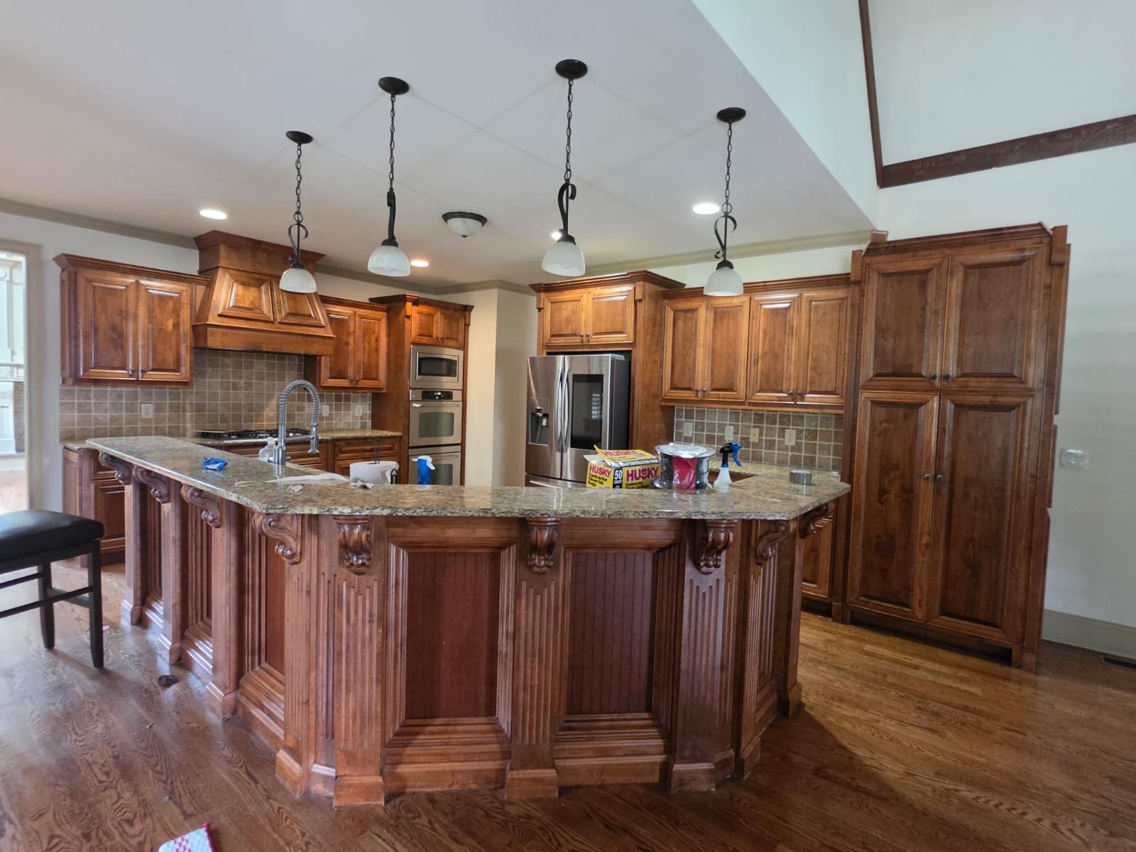 Kitchen with wooden cabinets, granite countertop island, stainless steel refrigerator, double ovens, and pendant lighting.