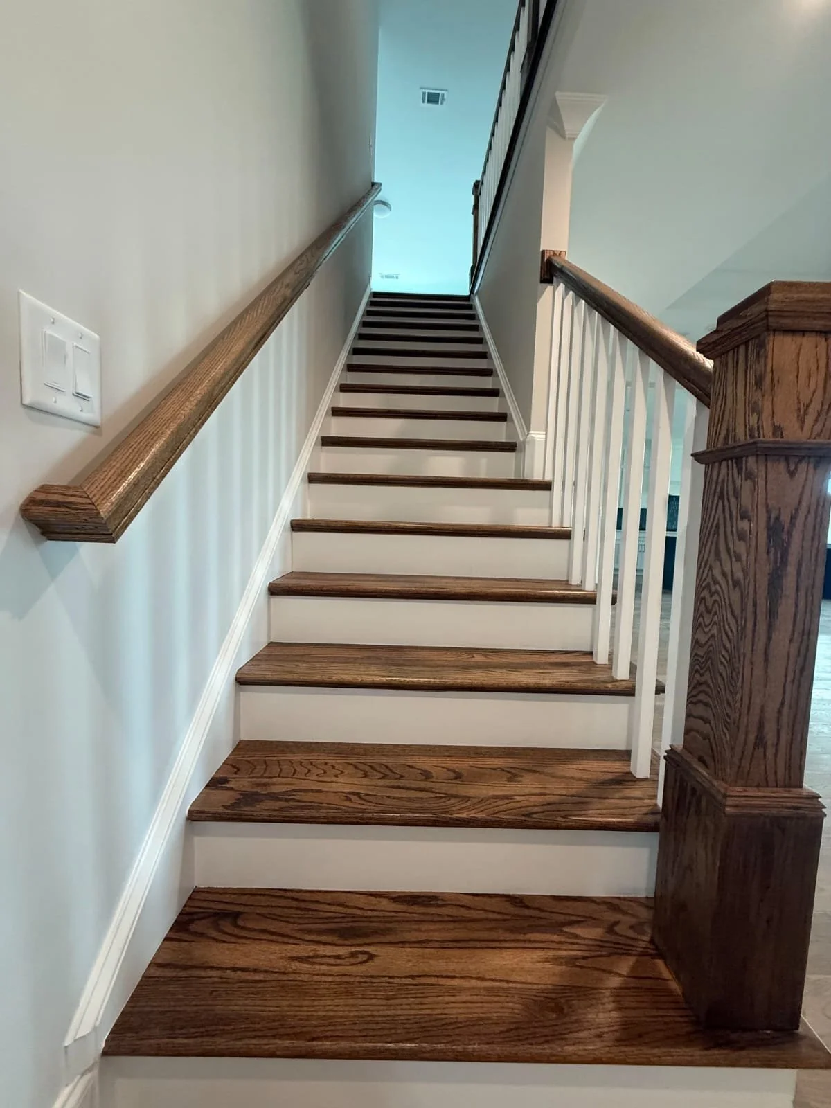 Freshly renovated staircase with wooden treads, white risers, and a dark wood handrail on the left side.