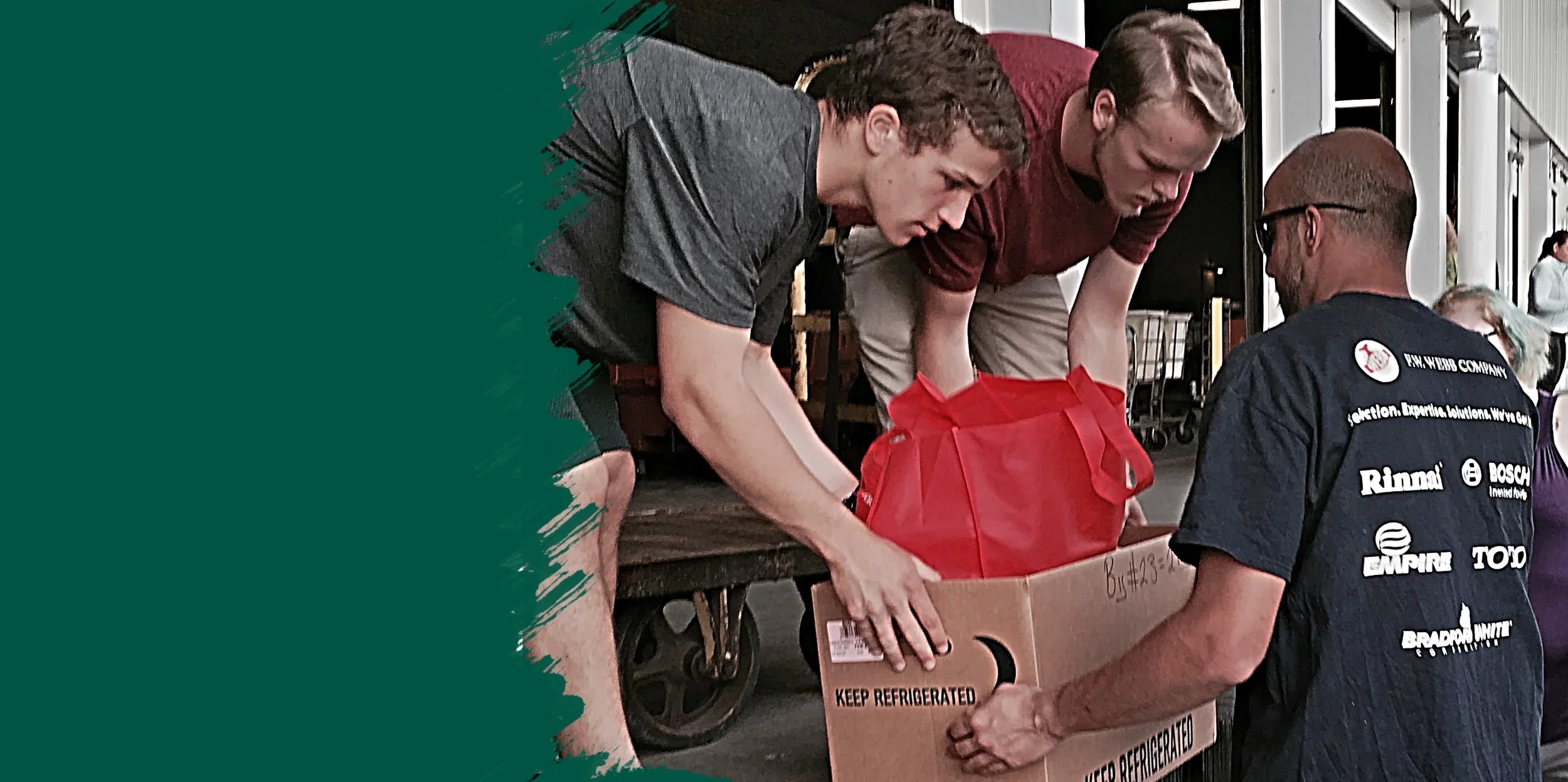 Two young men passing a box of canned goods to another male volunteer