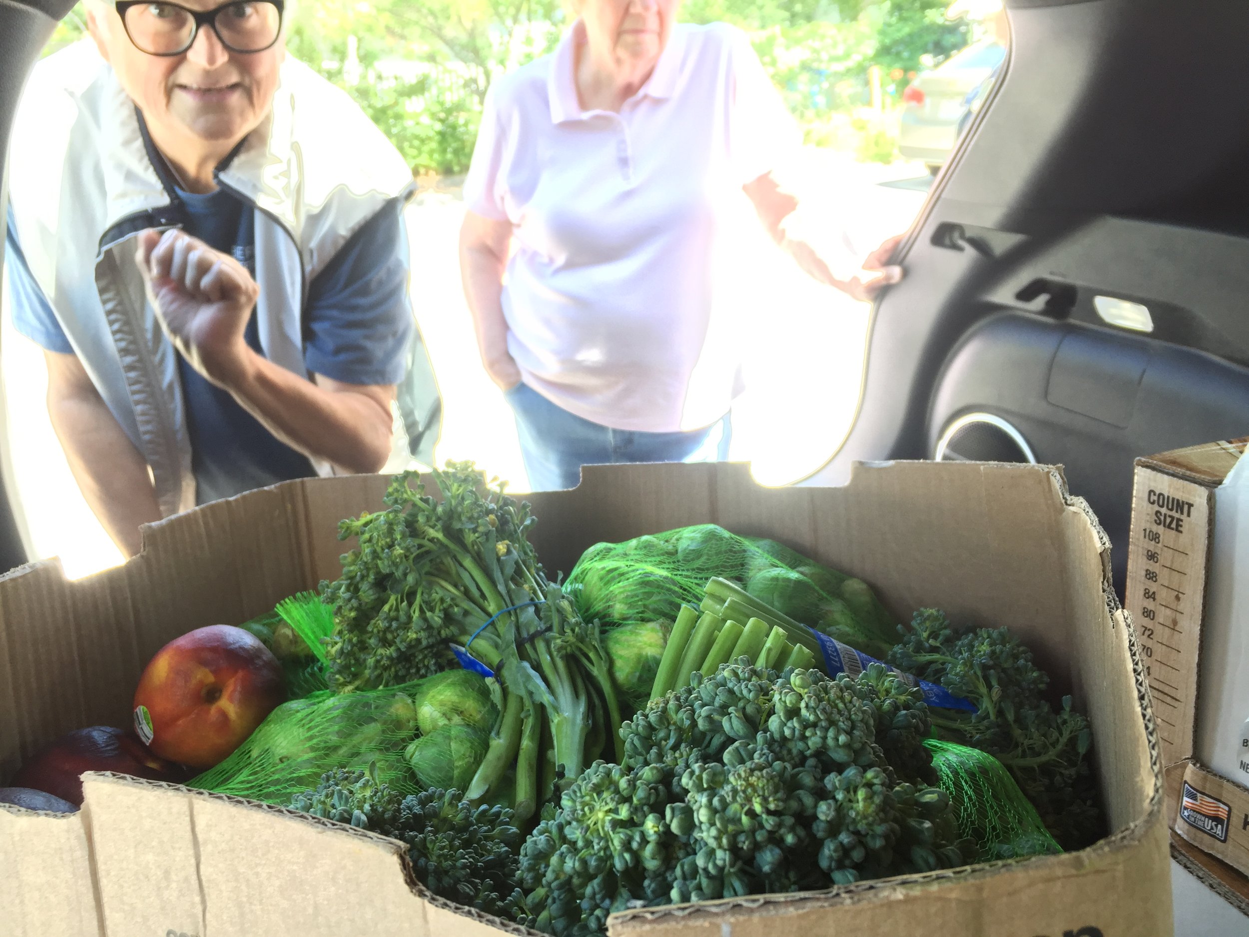 a woman peering into the back seat of a car with a box of vegetables on it