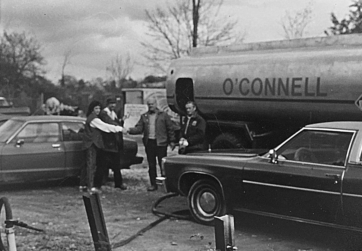 Photo of a meeting taking place in front of an oil truck showing "O'Connell" on the side.