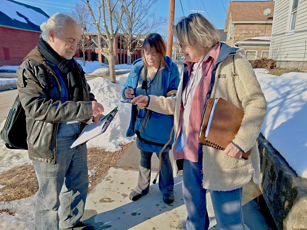 A man with a clipboard being directed by a woman with another woman in the background