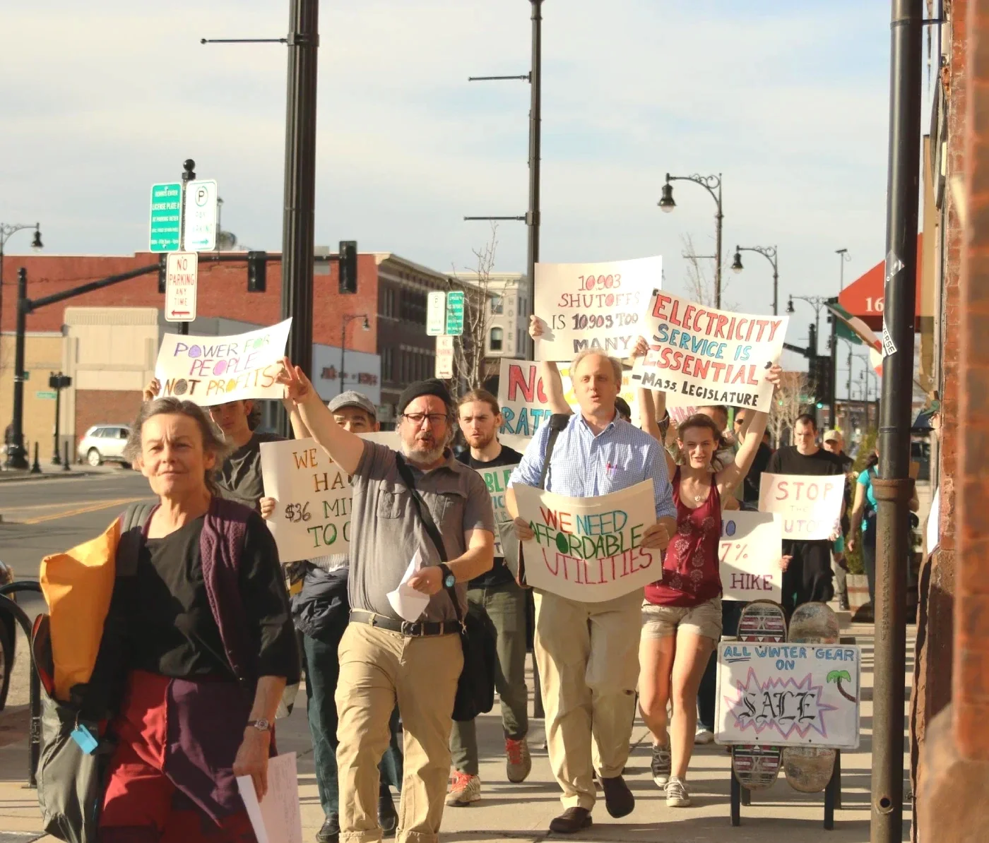 A march of WMLA members and volunteer with signs that read "We Need Affordable Utilities" and other similar messages.