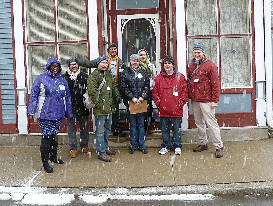 Eight people standing in front of a storefront in the snow wearing jackets and holding clipboards