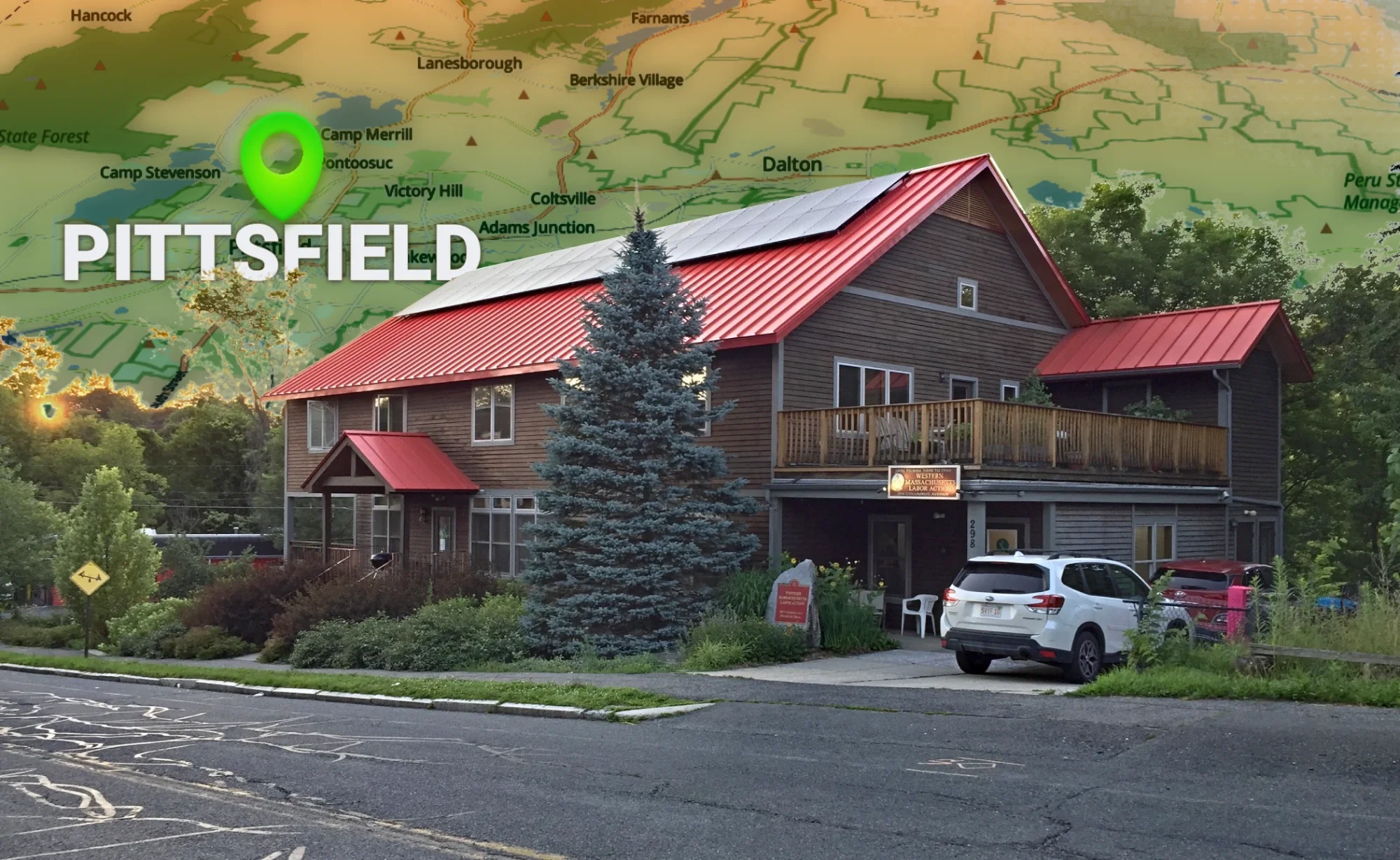 Photo of WMLA Office Central, a big, brown wood, two-story house with a red metal roof  with solar panels on it, with a map of Berkshire County in the background