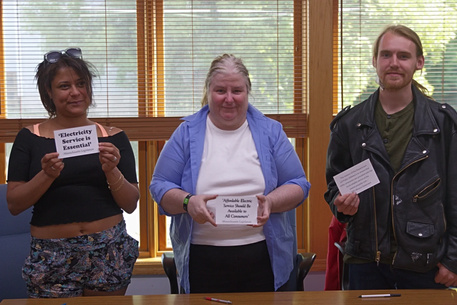 three people holding up postcards that say "Electricity Service is Essential"