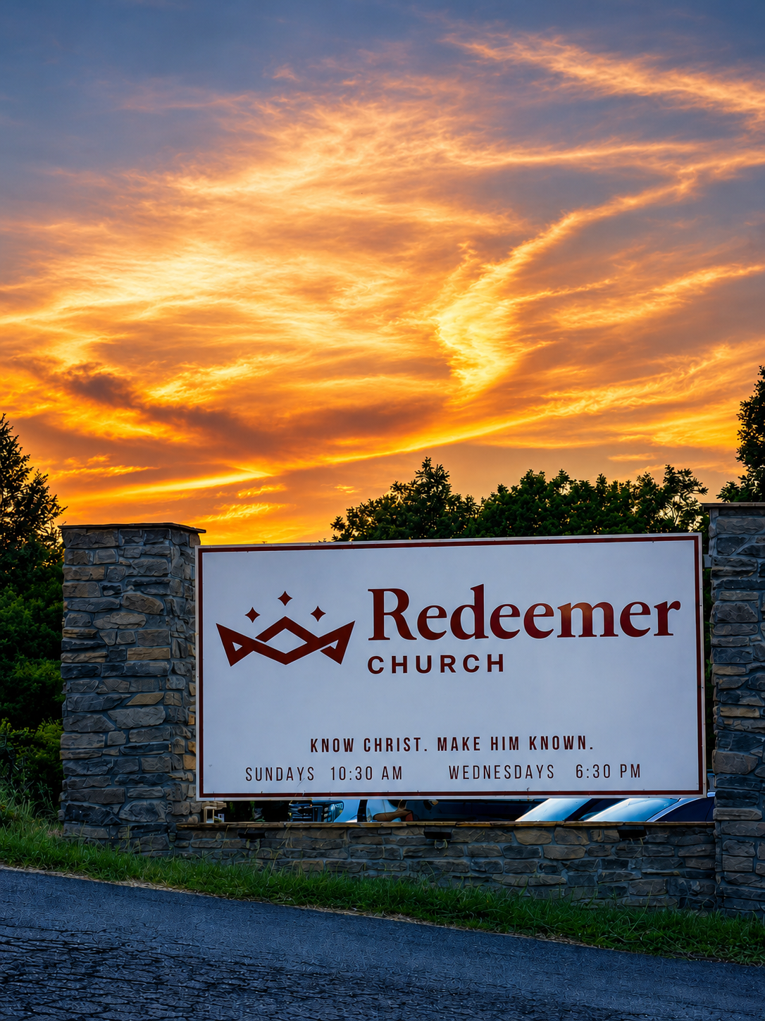 Sign for Redeemer Church with tagline 'Know Christ. Make Him Known.' and service times on a stone wall, with a sunset sky in the background.