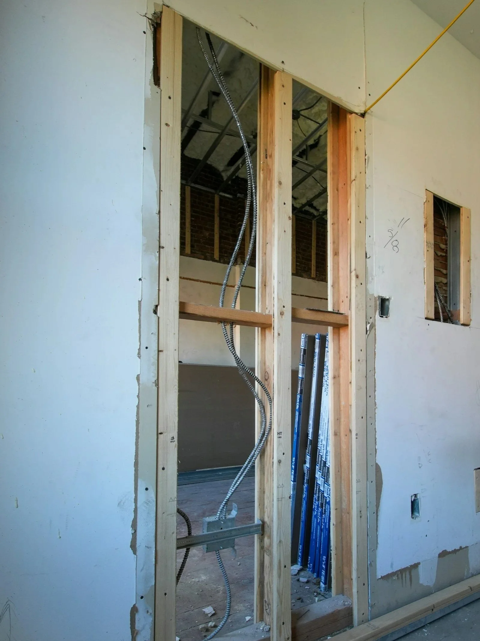 Partially constructed interior wall with exposed wooden studs, electrical wiring, and metal pipes, indicating ongoing building or renovation work.