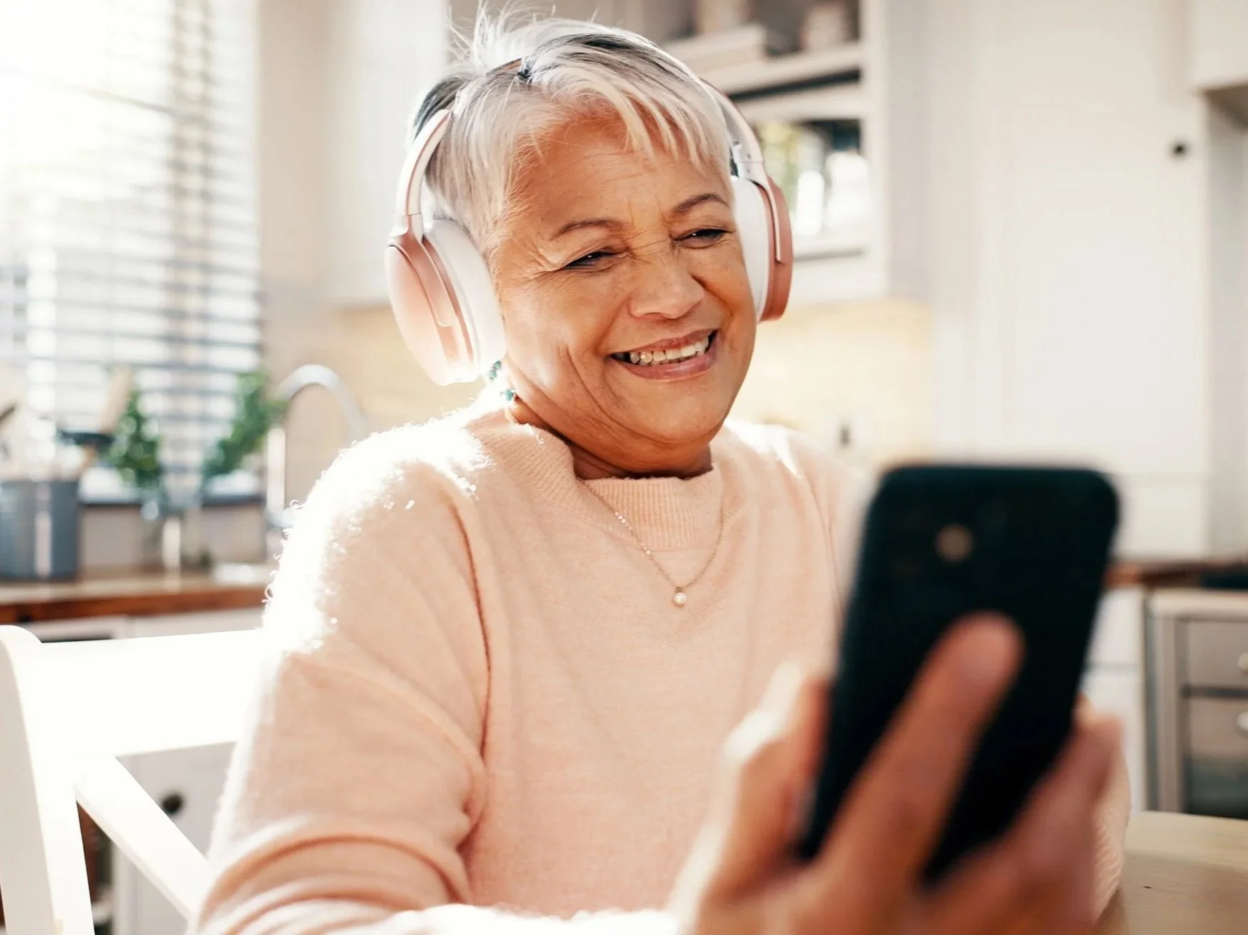 A mature woman enjoys a telehealth session with The Dietitian's Office using her cell phone and headphones.