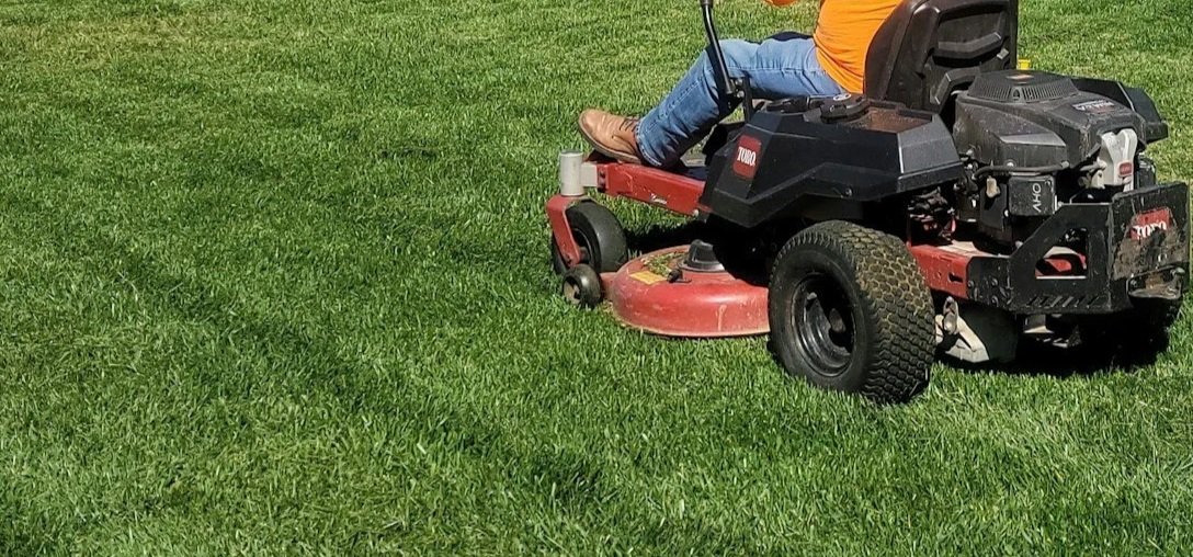 Person riding a red and black riding lawn mower on a green grassy field.