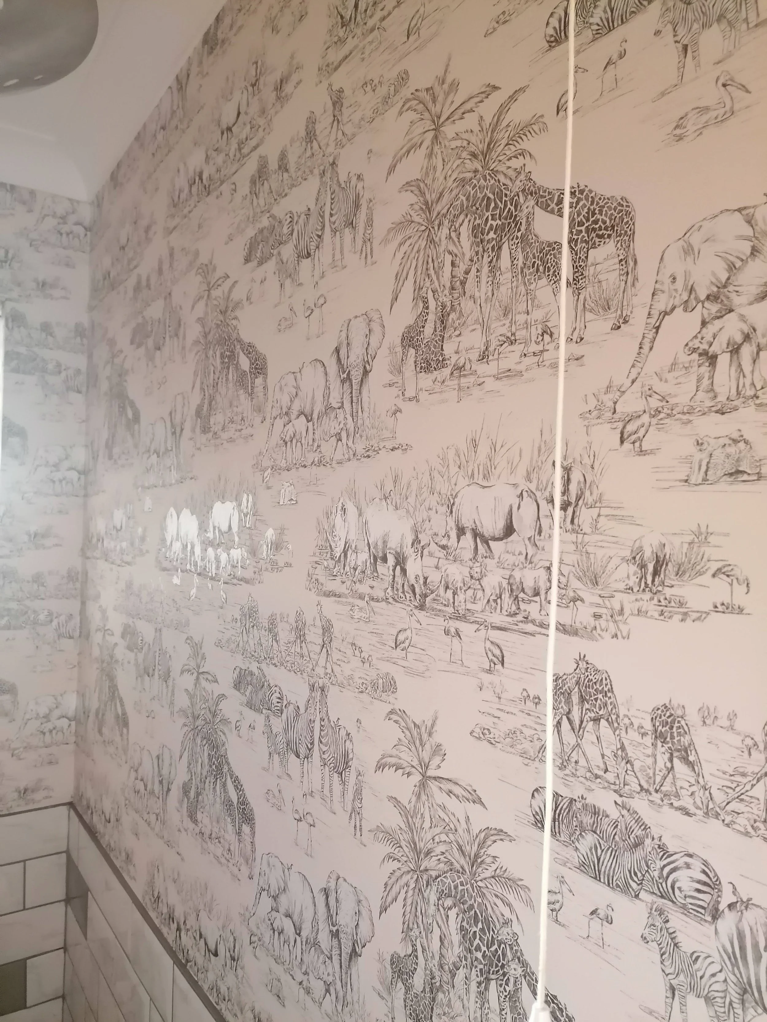 Black and white mural of African safari scene with various animals including giraffes, elephants, zebras, and birds, with palm trees and grassy landscape.