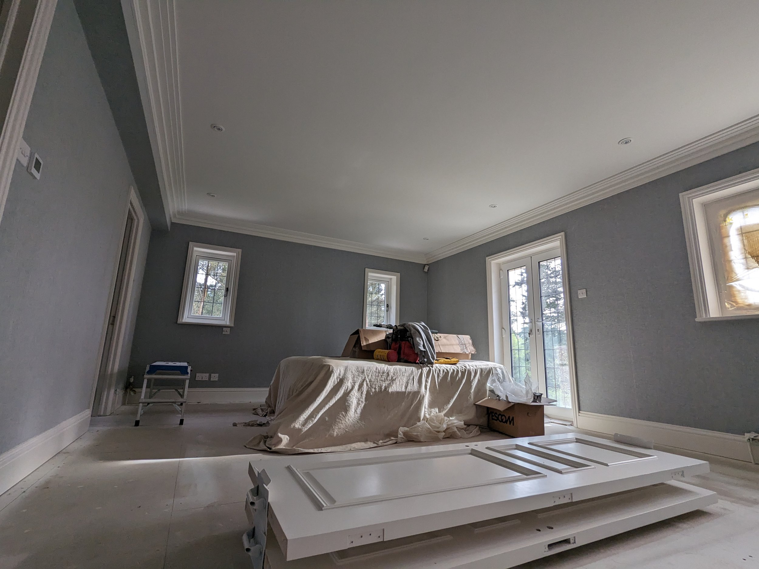 Living room under renovation with window coverings, a plastic-covered furniture, and tools.