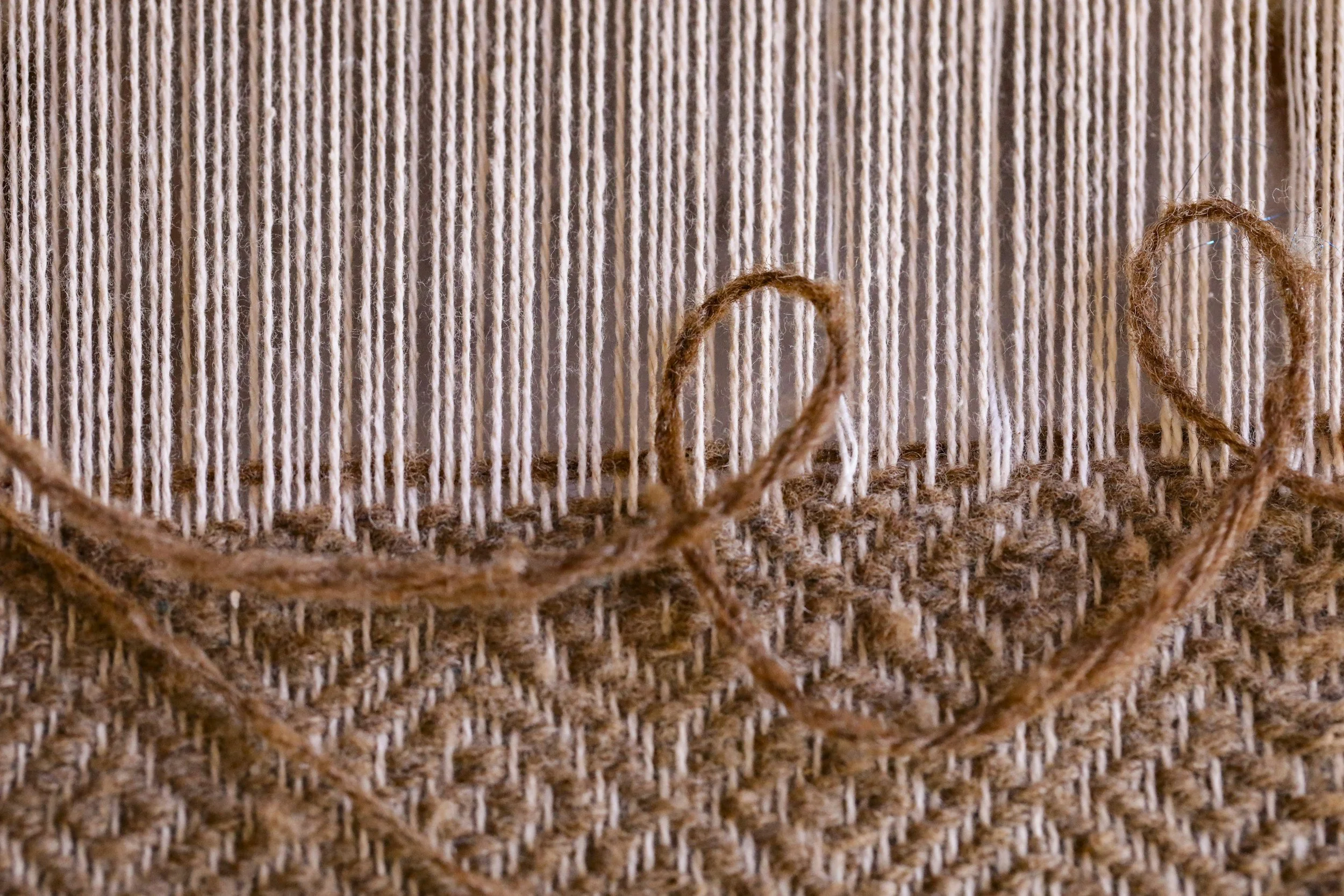 Close-up of a textured surface with vertical strands of light brown yarn and brown twine intertwined at the bottom.