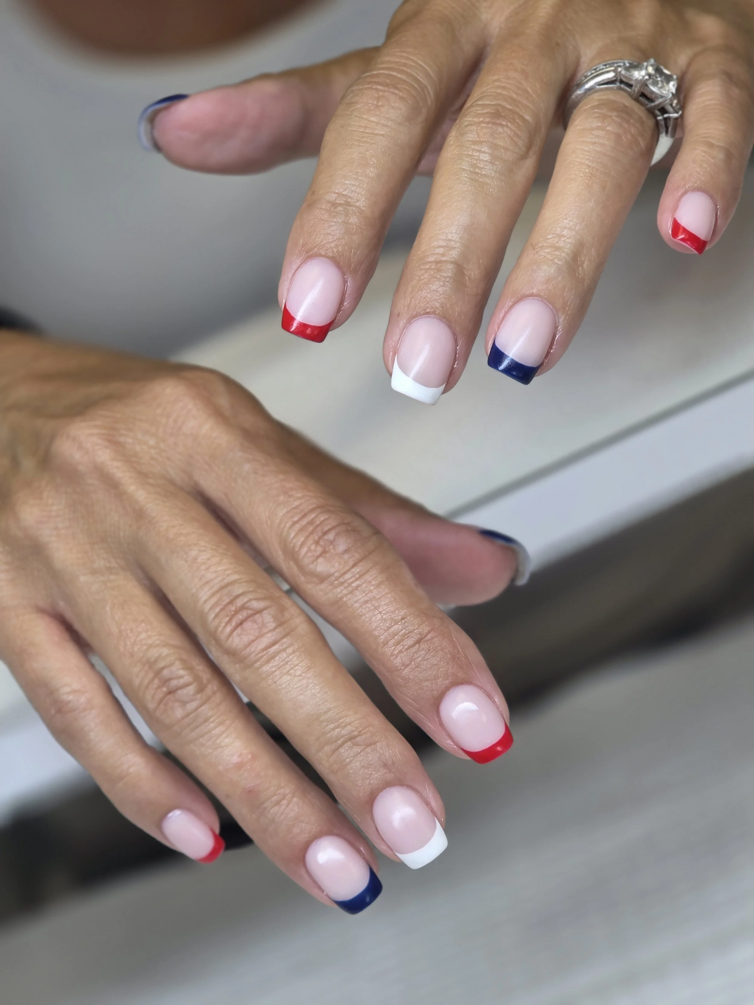 Close-up of hands with French manicured nails in red, white, and blue, and a silver ring on the finger.