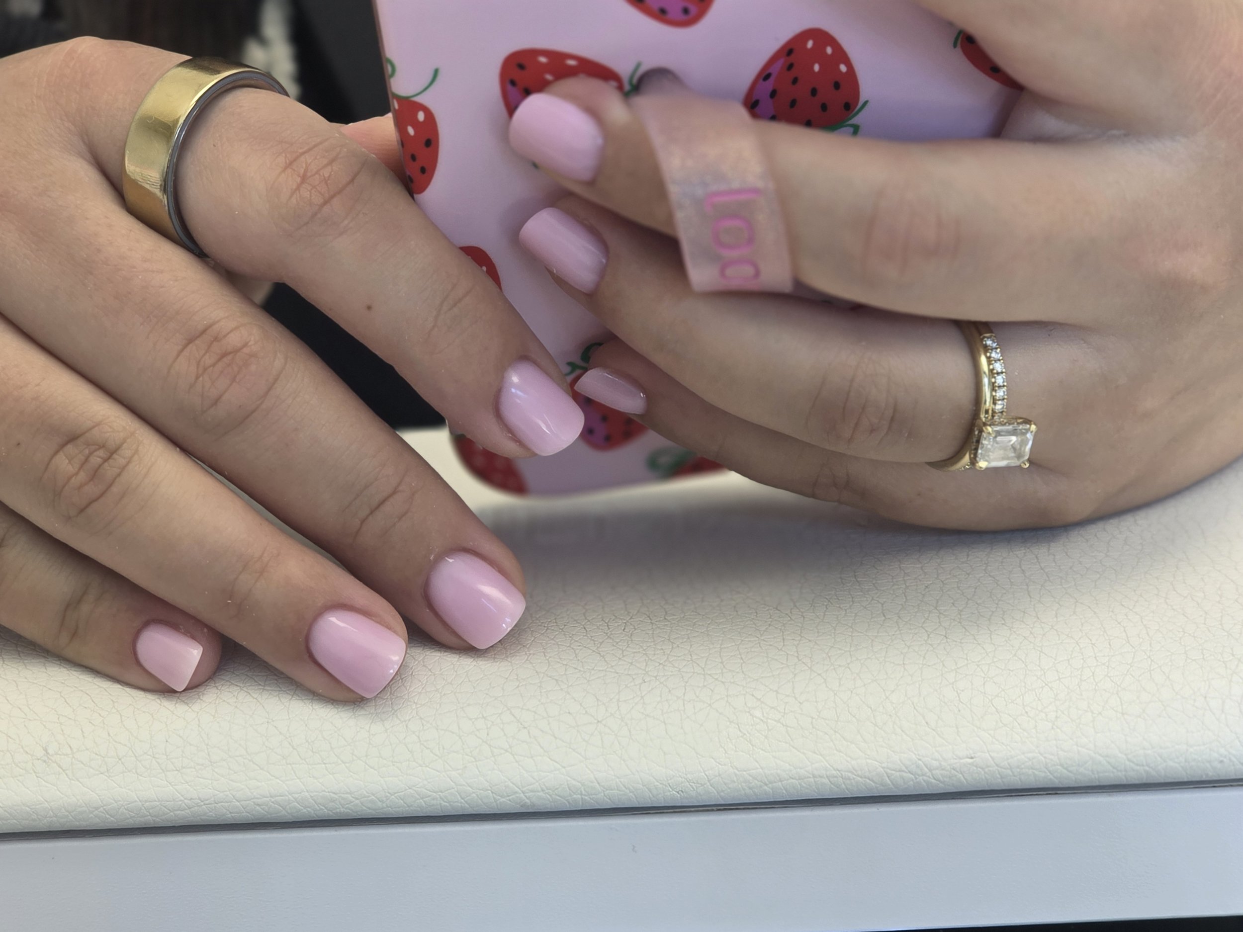 Close-up of hands with manicured nails, wearing rings, holding a shopping bag with strawberry print.