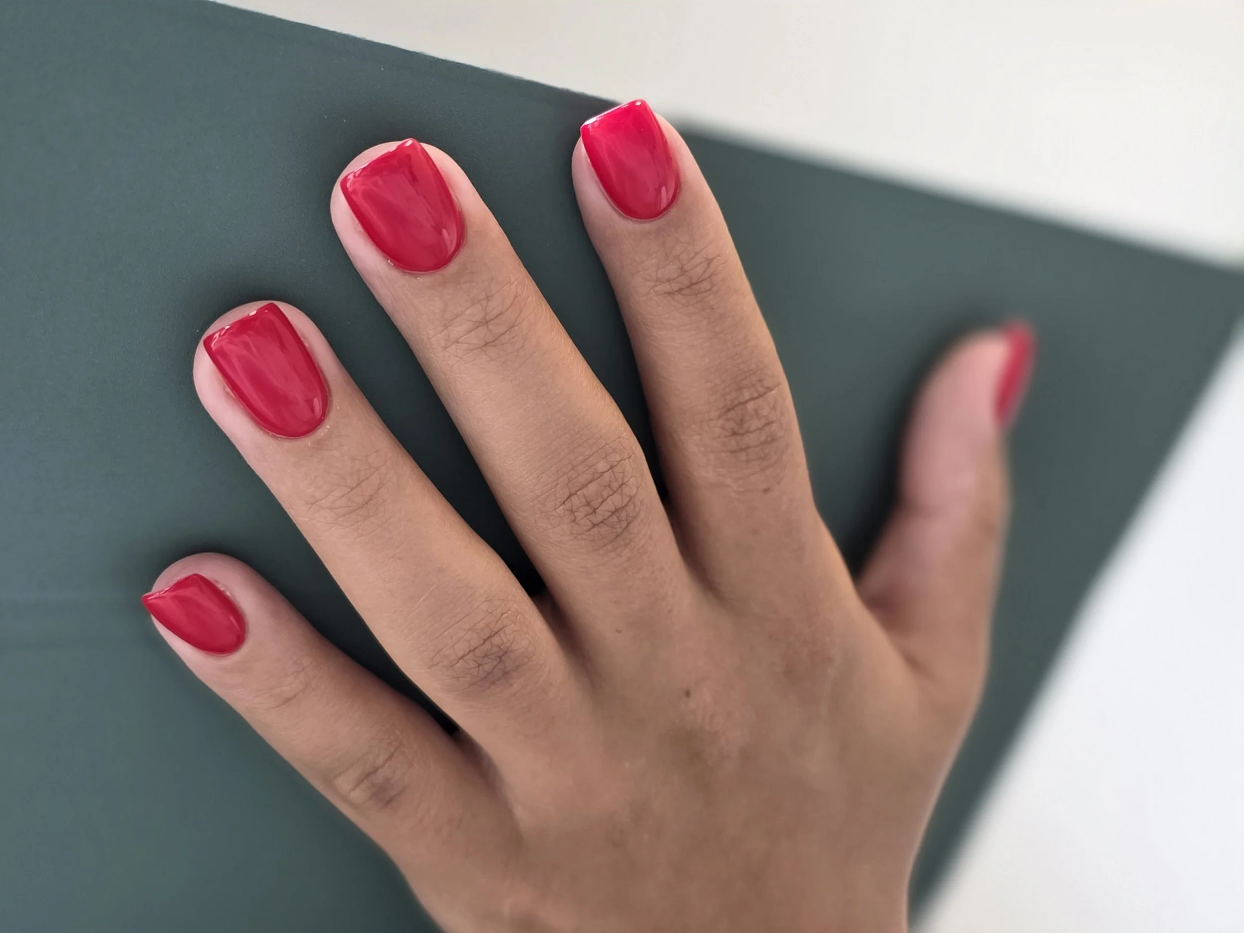 Close-up of a person's hand with neatly painted bright red fingernails resting on a dark green surface.