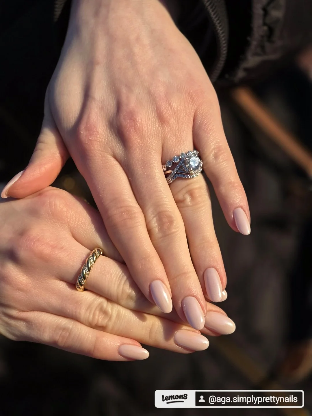 Close-up of two hands with rings, one with a diamond engagement ring and wedding band, the other with a gold wedding band, resting together.