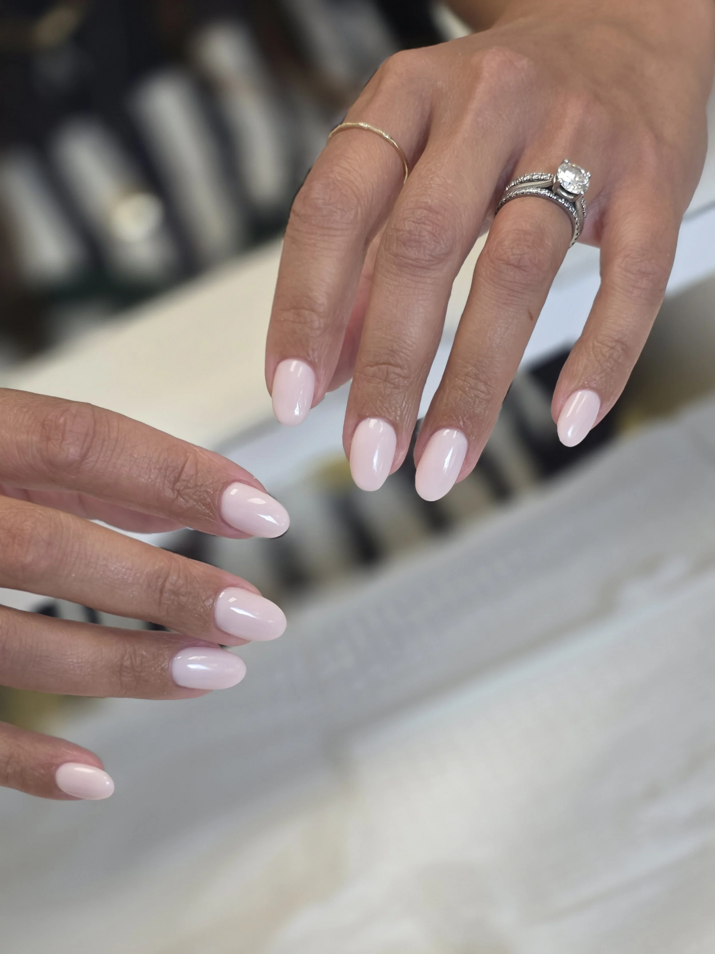 Close-up of a woman's hand with a diamond engagement ring and a wedding band, showing well-manicured nails and a gold ring on the pinky finger.