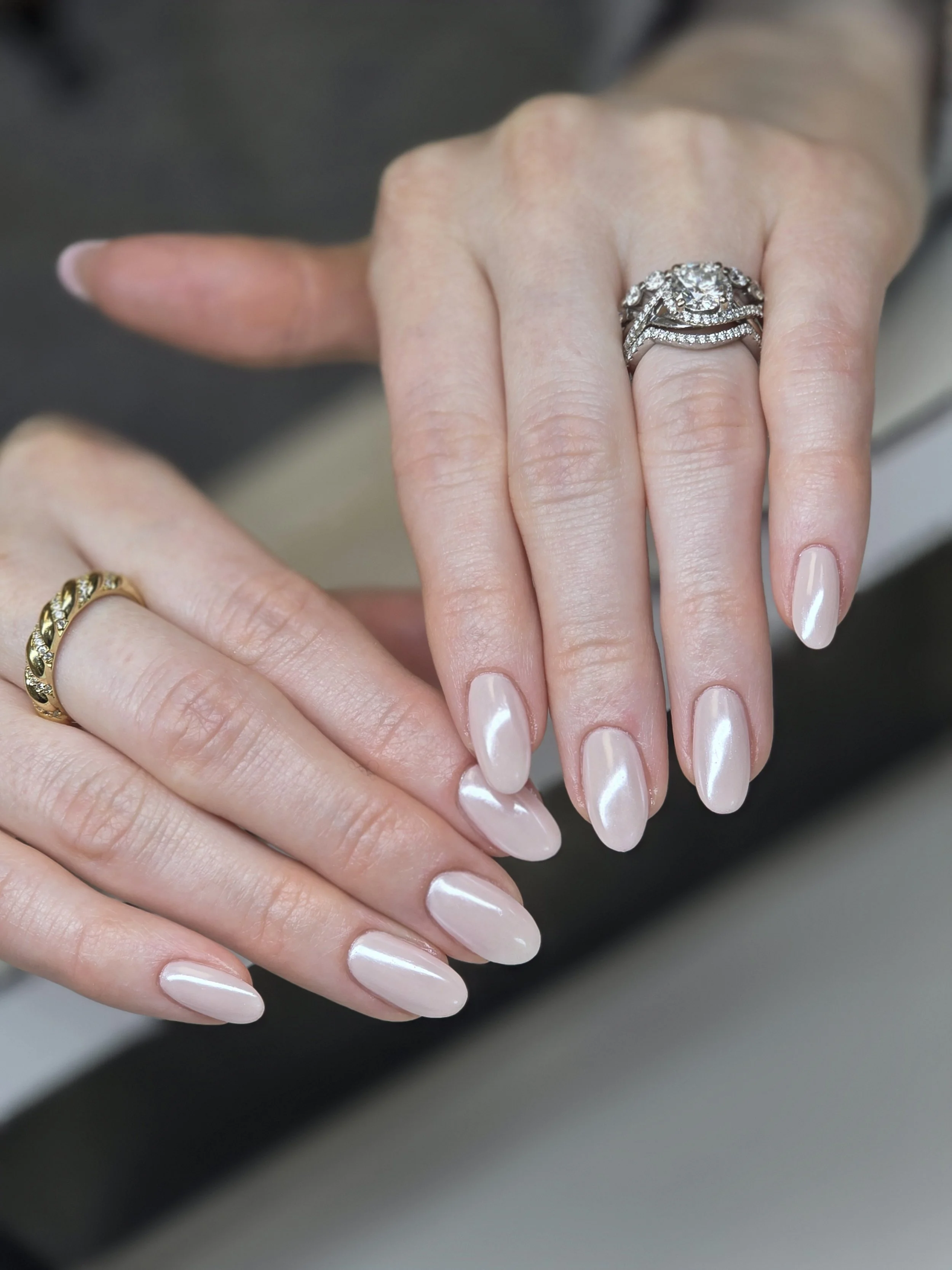 Close-up of a woman's hand with manicured nails and a large diamond engagement ring, and another hand with a gold ring, both resting on a black surface.