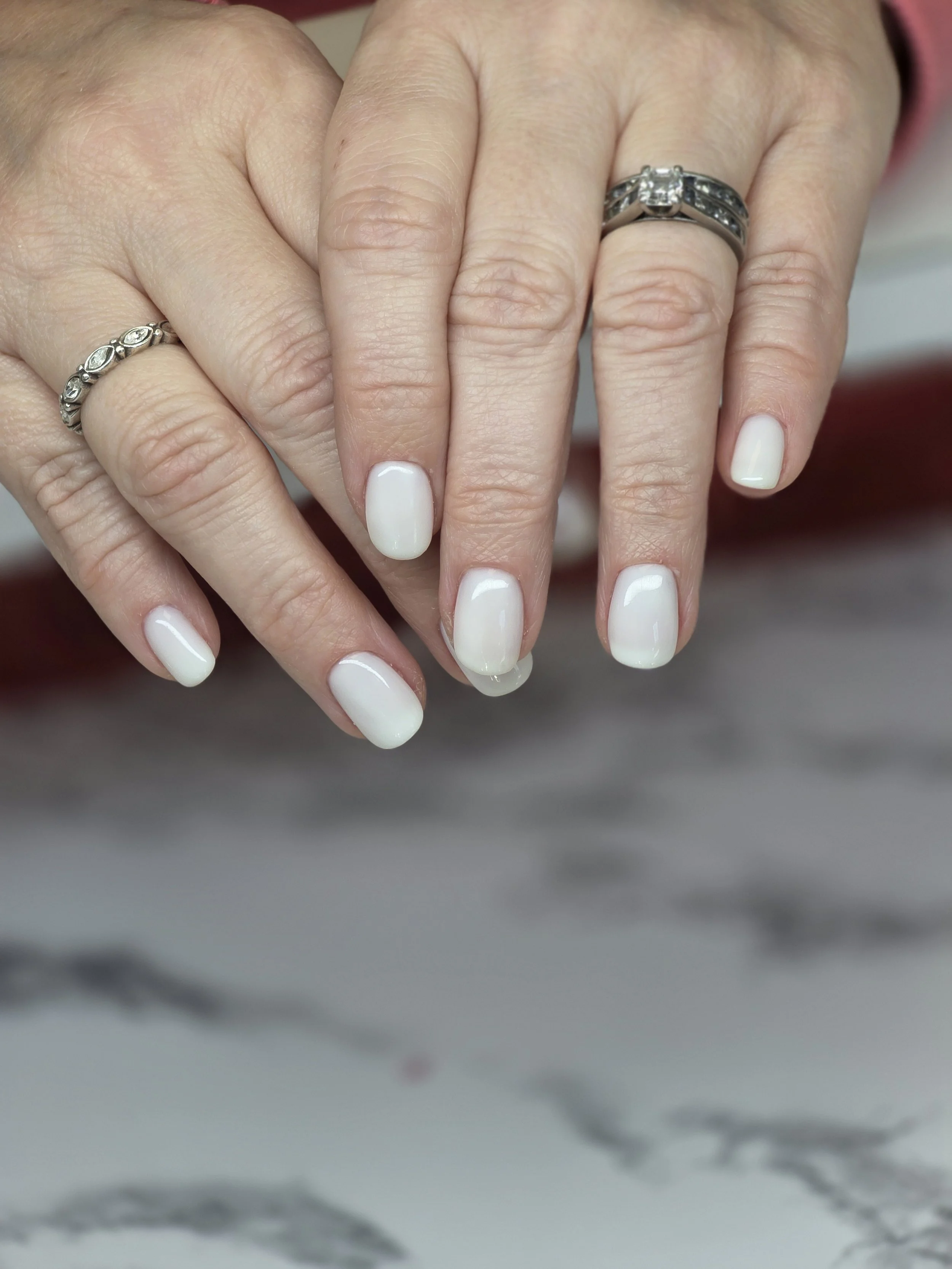 Close-up of a person's hands showing off wedding rings on each finger. The nails are painted white.