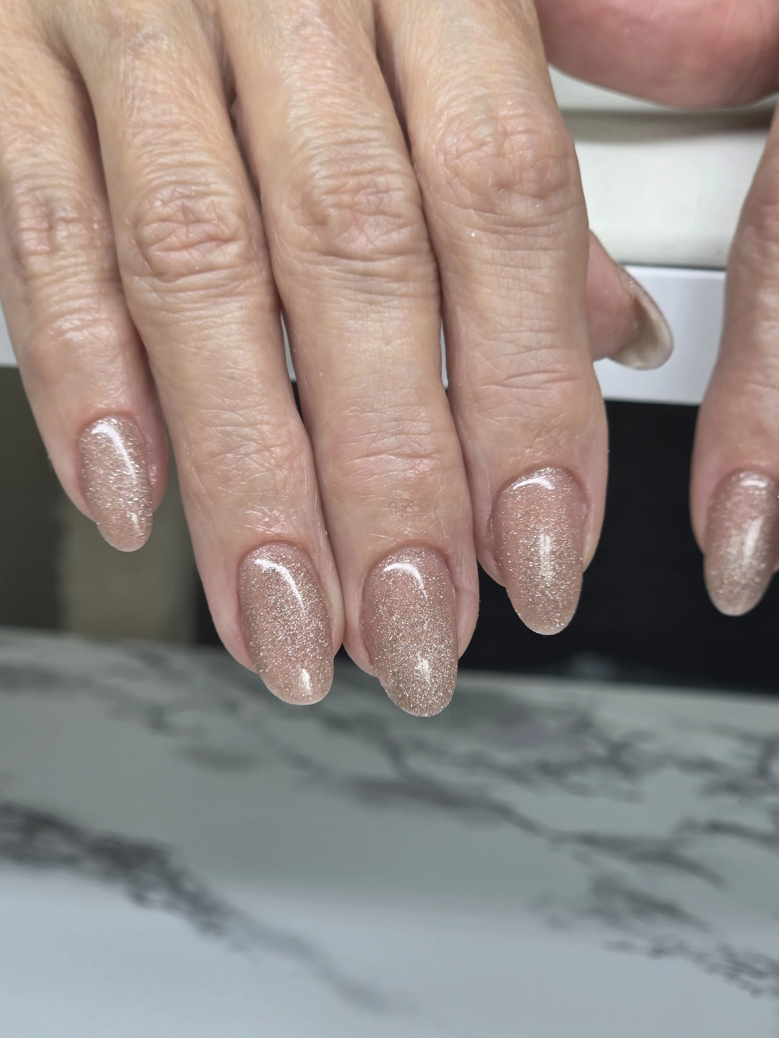 Close-up of hands with manicured nails, painted with glittery, light pink nail polish.