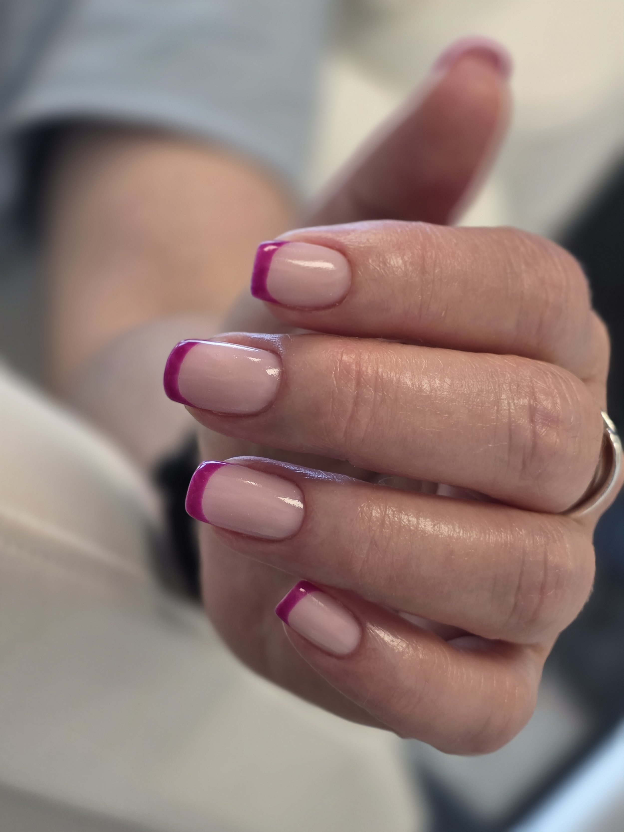 Close-up of a person's hand with neatly manicured nails, featuring a French tip design with a pink rim, holding a mirror.