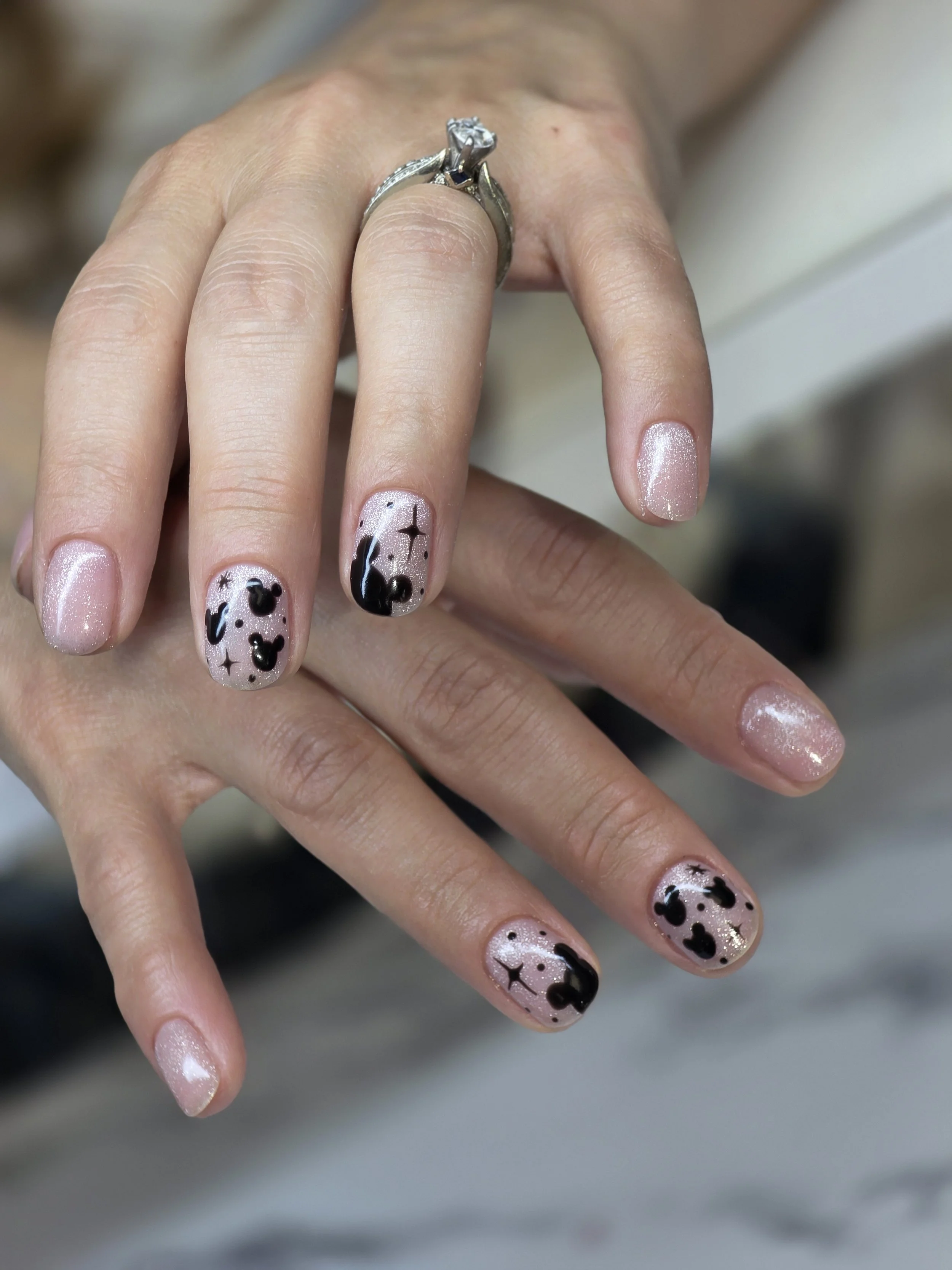 Close-up of a hand with manicured nails and a diamond engagement ring on the ring finger, featuring black and white nail art with Mickey Mouse designs.