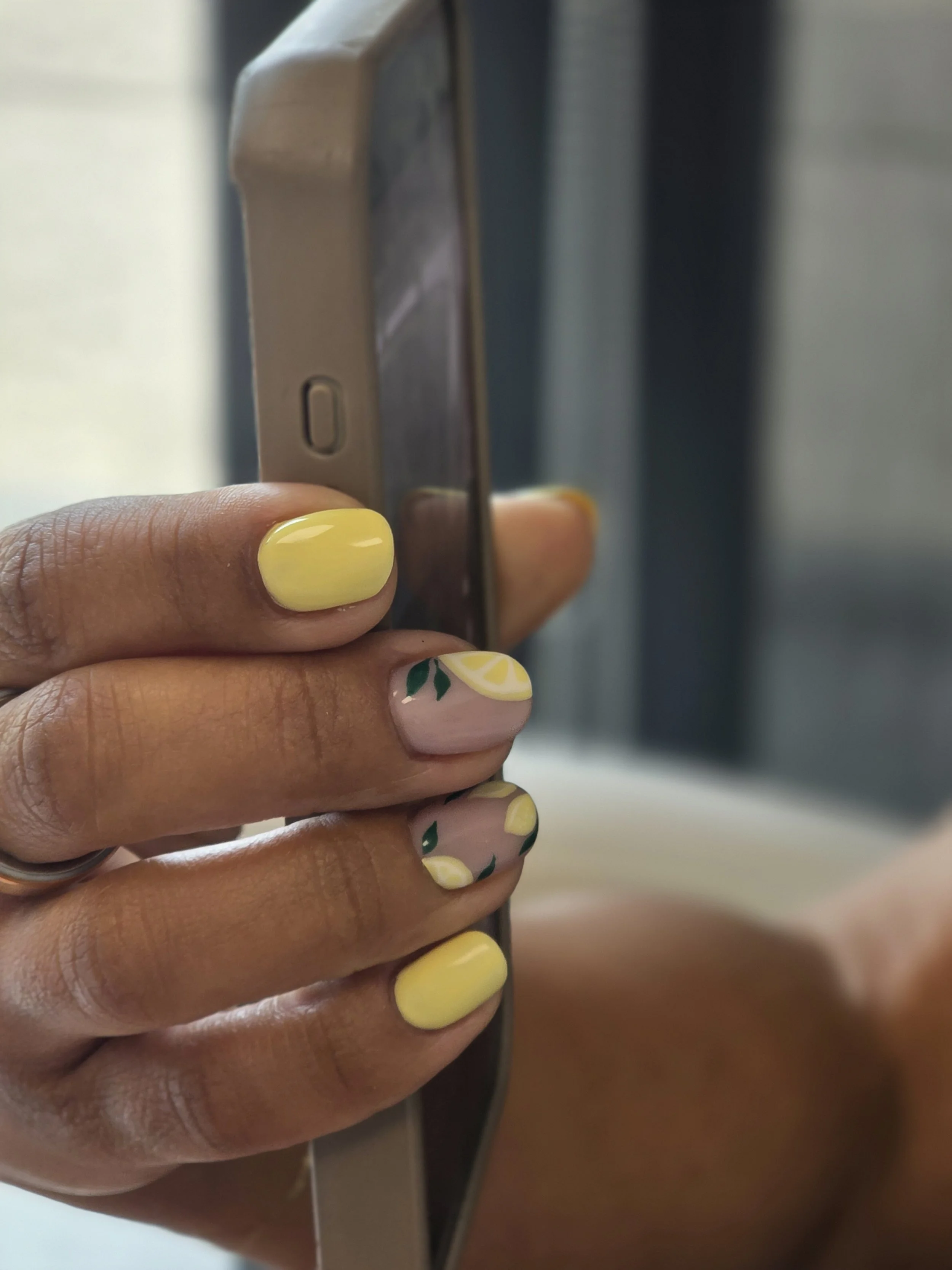 Close-up of a person's hand with yellow and lemon-patterned nails, holding a smartphone next to what appears to be a keypad or scanner.