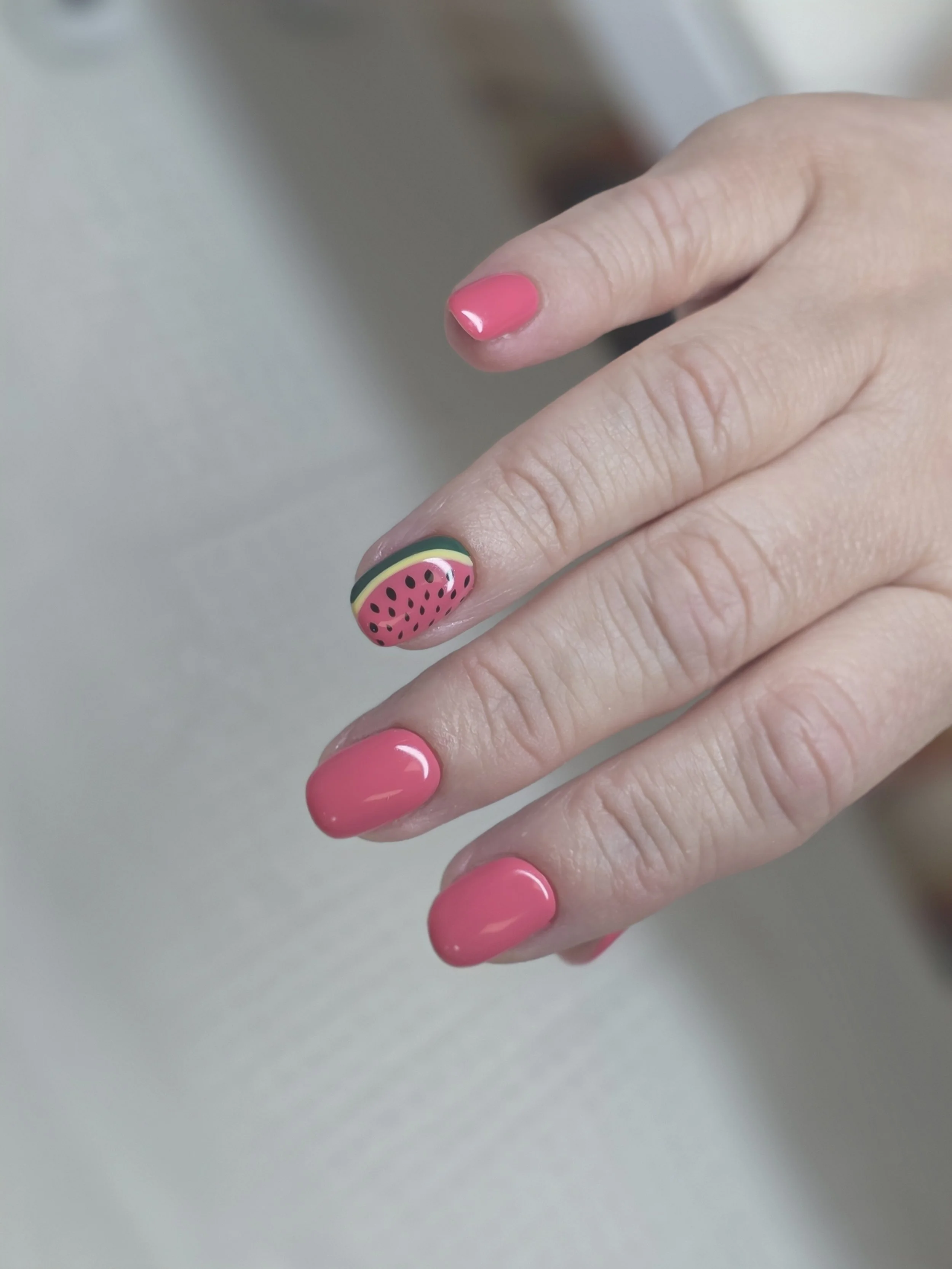 Close-up of a person's hand with pink and watermelon-themed nail art.