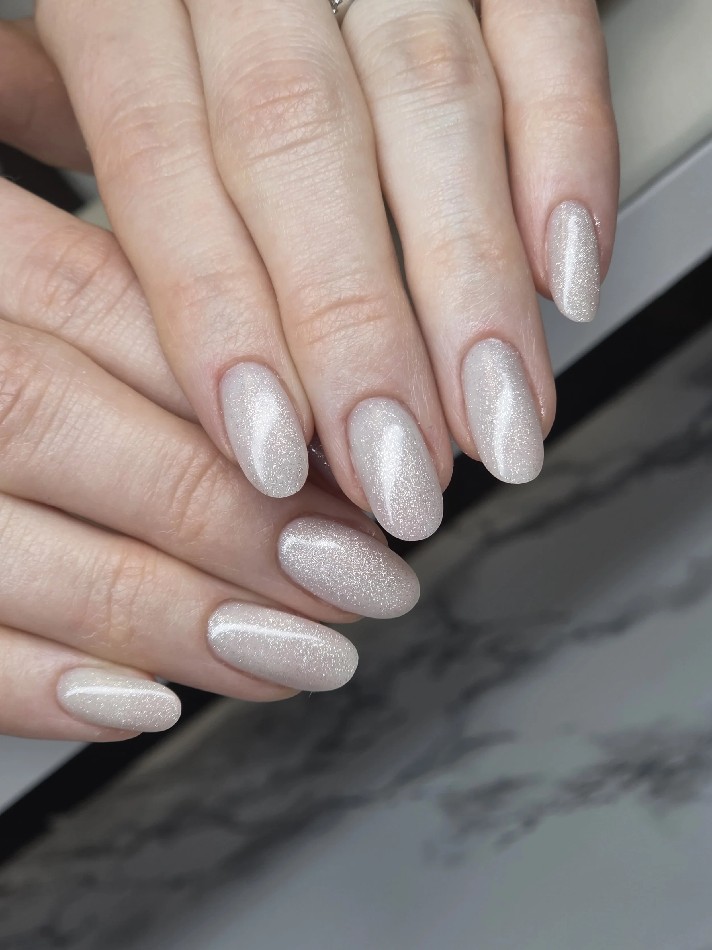 Close-up of a hand with manicured nails painted in a shimmering, light pearlescent color.
