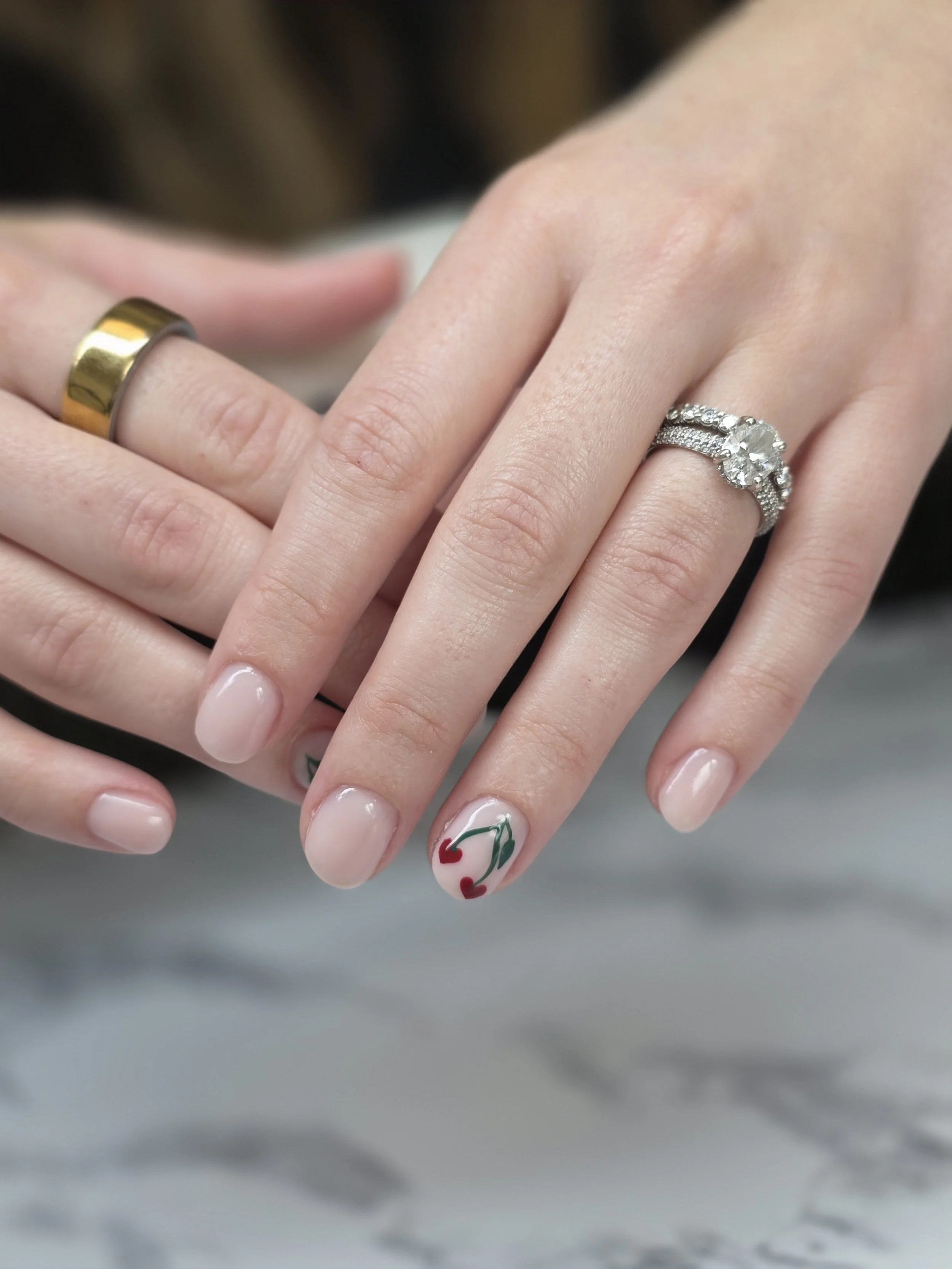 Close-up of two hands with wedding rings and manicured nails, one with painted nails decorated with green holly and red hearts, the other with a large diamond engagement ring and a plain gold wedding band.