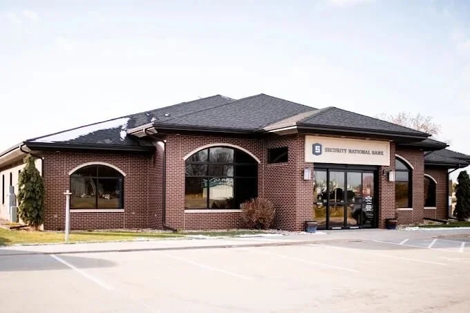 A brick bank building with a sign that reads 'Security National Bank,' large windows, and a parking lot in front.