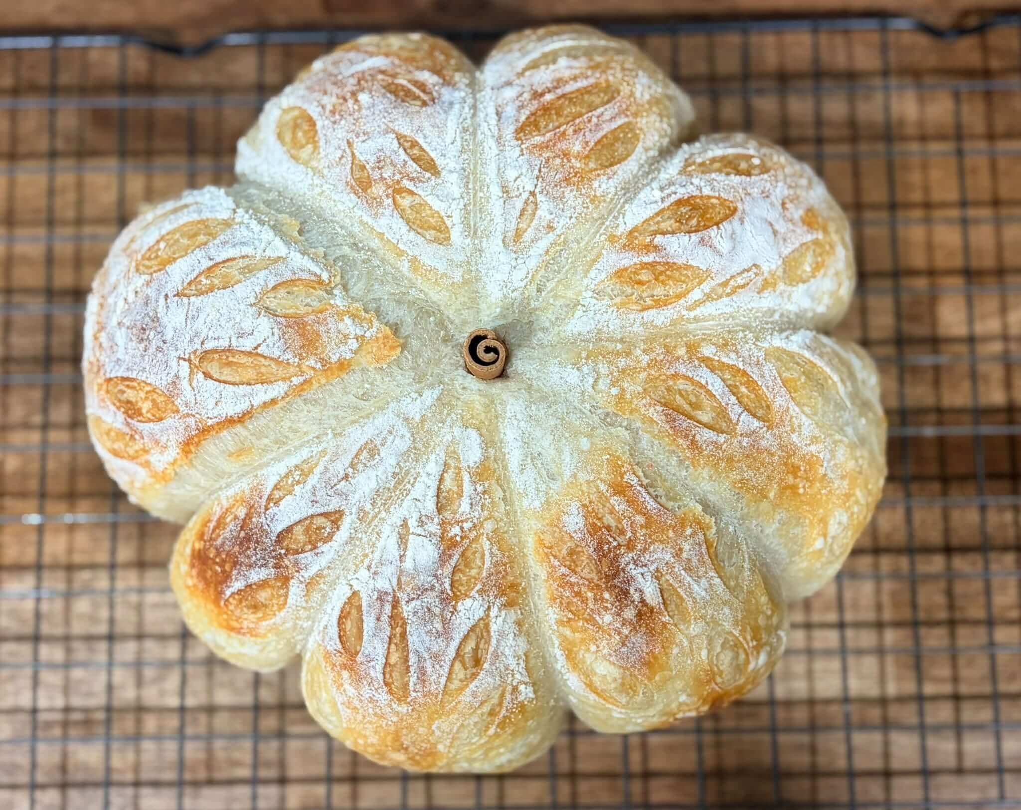Close-up of a freshly baked loaf of bread with a white flour dusting and almond-shaped toppings on a cooling rack.