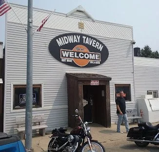 Exterior of Midway Tavern with a welcome sign, a motorcycle parked outside, and a person walking near the entrance.