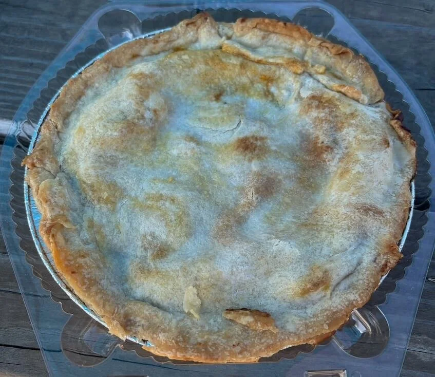 A large, round, baked pie with a golden-brown crust on a clear plastic plate.