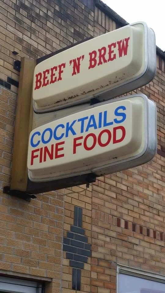 Vintage restaurant sign on brick wall reading 'Beef 'n' Brew' and 'Cocktails Fine Food'.
